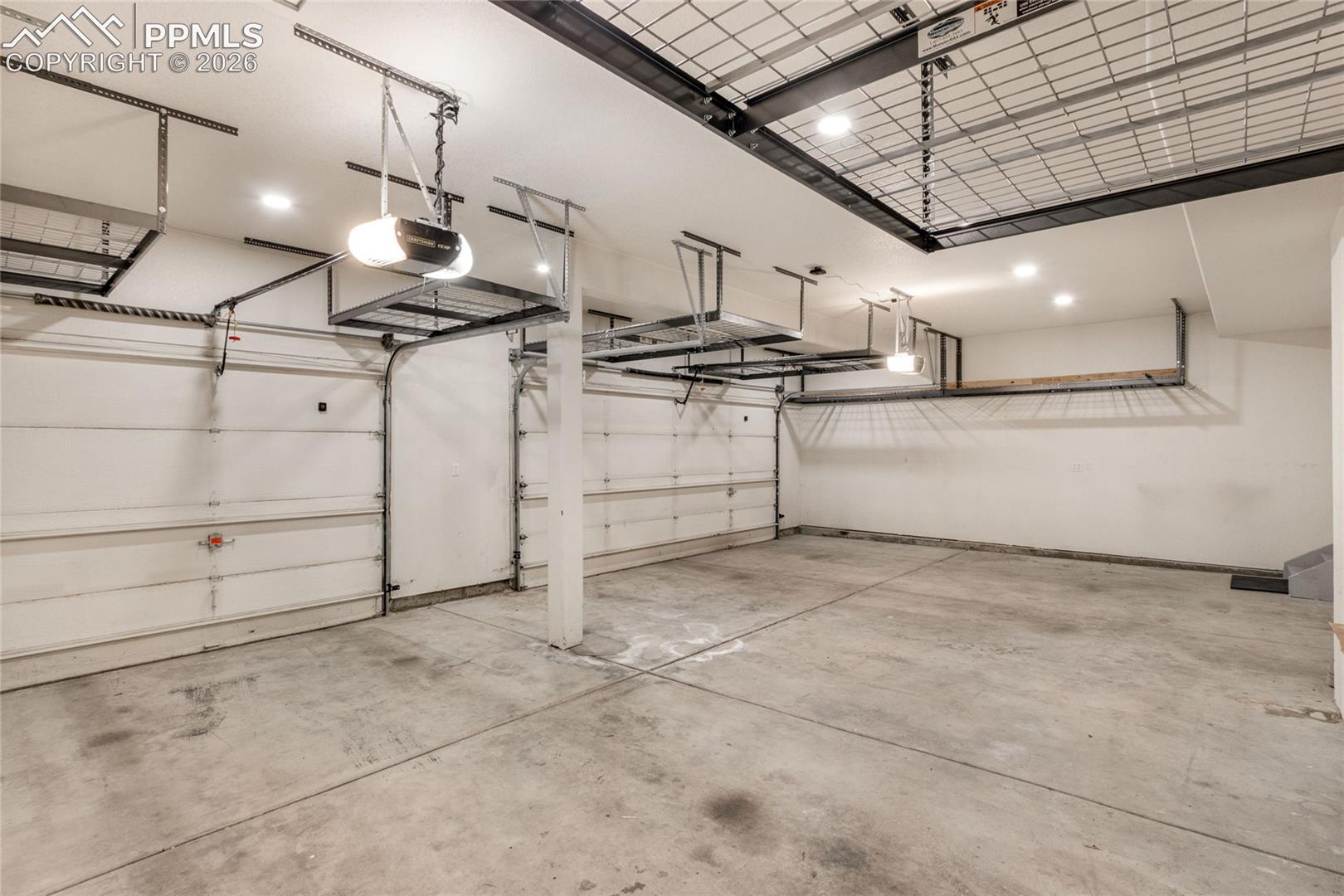 Spacious 3 car garage with multiple overhead storage racks, two garage doors, and recessed ceiling lighting and door to backyard