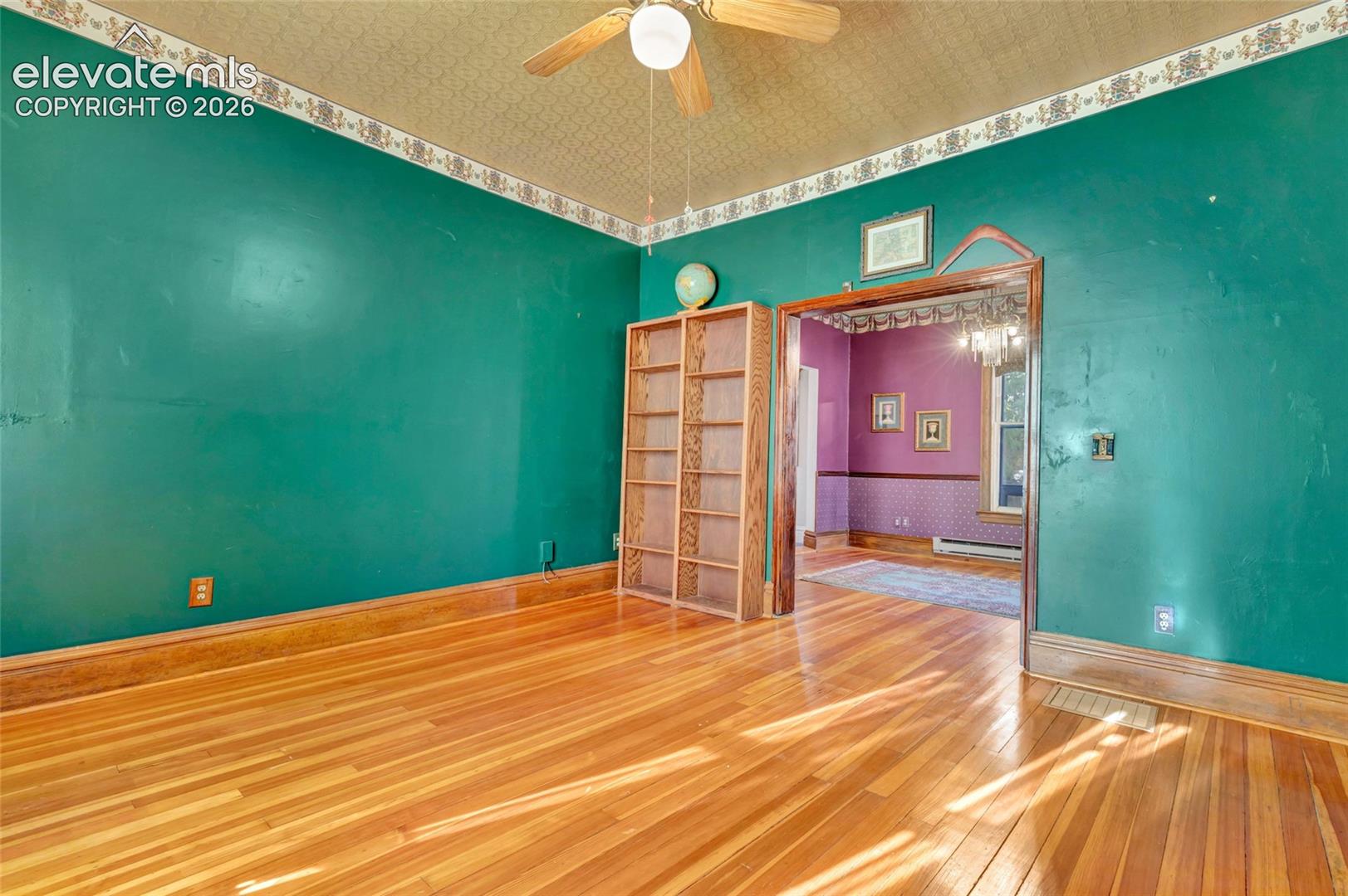 Wood-finish flooring, built-in wooden shelving, ceiling-mounted paddle fan, and decorative crown moulding