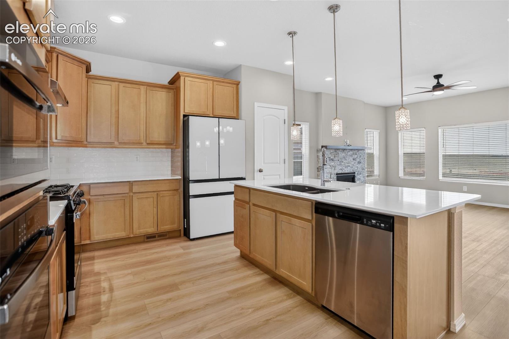 Open-concept kitchen featuring light wood-finish cabinetry, a white subway tile backsplash, and stainless steel appliances