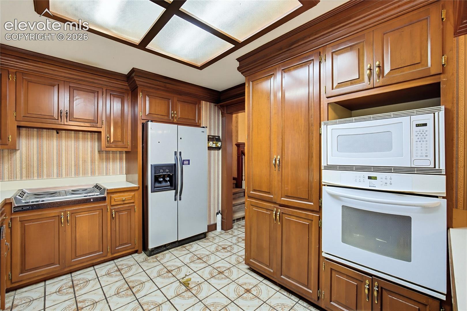 Wood-tone cabinetry, tiled flooring, integrated wall oven, built-in microwave, and a side-by-side refrigerator