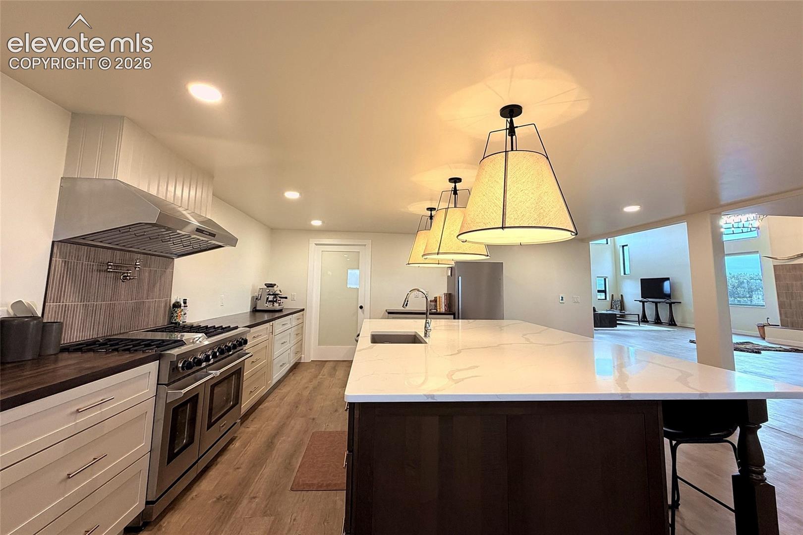 Kitchen featuring a large central island with a stone-surface countertop, stainless steel professional-style range, wood-finish flooring, recessed lighting, and a built-in exhaust hood