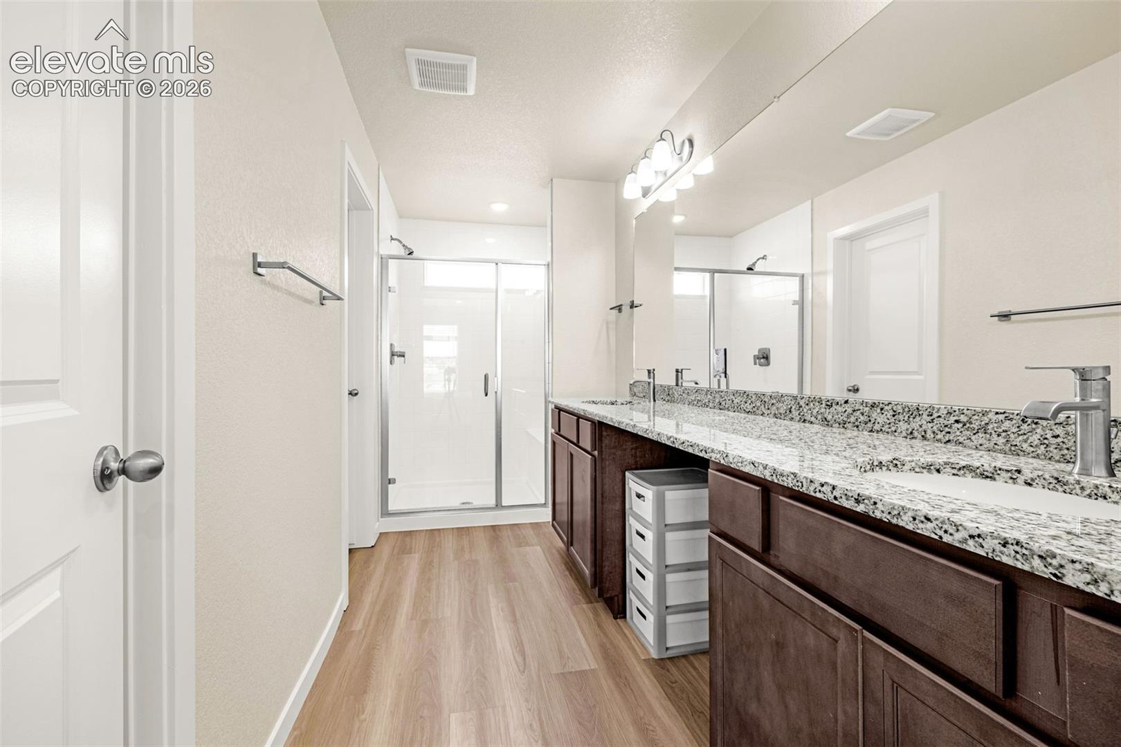 Dual vanity with granite-style countertop and undermount sinks, wood-finish cabinetry, and a glass-enclosed shower