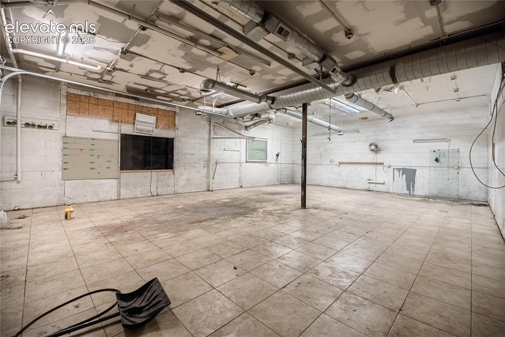 Exposed ceiling ductwork, concrete block walls, overhead fluorescent lighting, and large format floor tiling