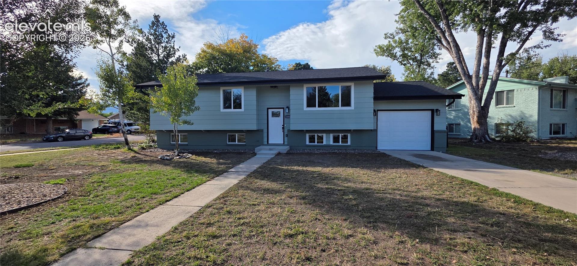 Split-level residence featuring a two-tone exterior, white-framed windows, an attached garage with a white door, and a concrete driveway