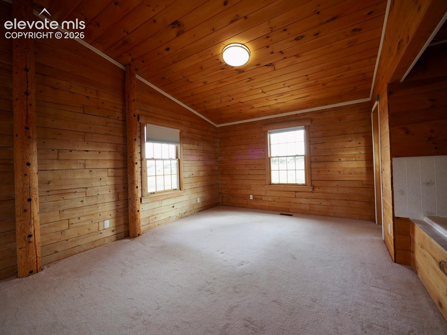 Interior space featuring horizontal wood-plank walls and ceiling, exposed vertical timber pillars, dual windows, and a flush-mount dome light fixture