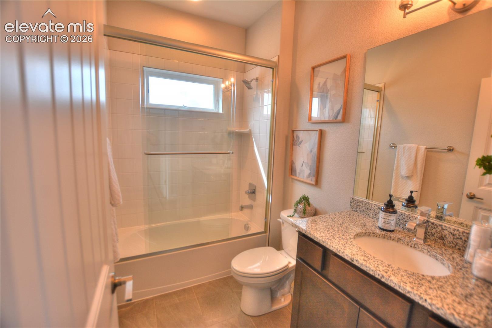 Contemporary bathroom featuring a granite-topped vanity with dual sink basins, framed mirror with integrated lighting, and a walk-in shower enclosure with sliding glass doors and tile surround
