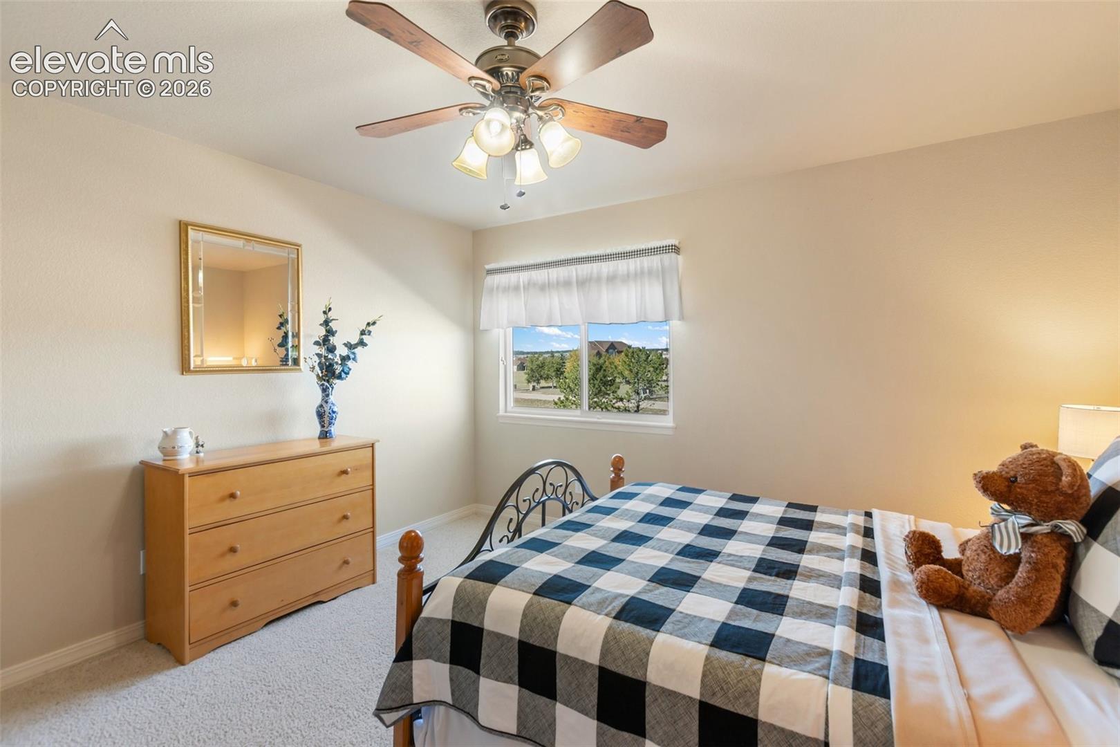 Neutral-toned walls, carpeting, a ceiling-mounted fan with integrated lighting, and a sliding window with a horizontal valance