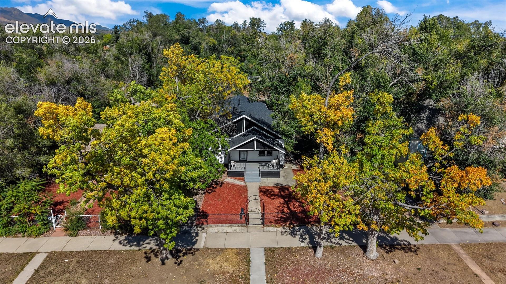 Gable roofline residence with a covered porch, surrounded by mature trees and a mountain backdrop