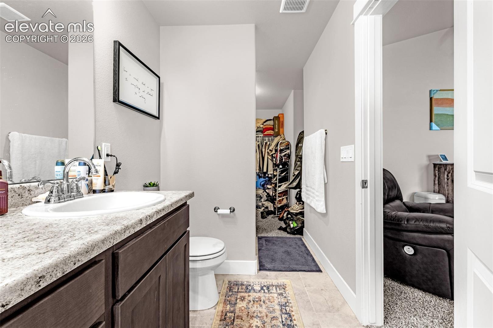 Bathroom featuring a wood-finish vanity with a light speckled countertop, undermount sink, and chrome faucet
