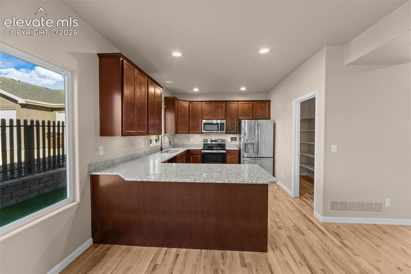 Kitchen featuring dark wood cabinetry, stone-surface countertops, stainless steel appliances, a peninsula island, and wood-finish flooring