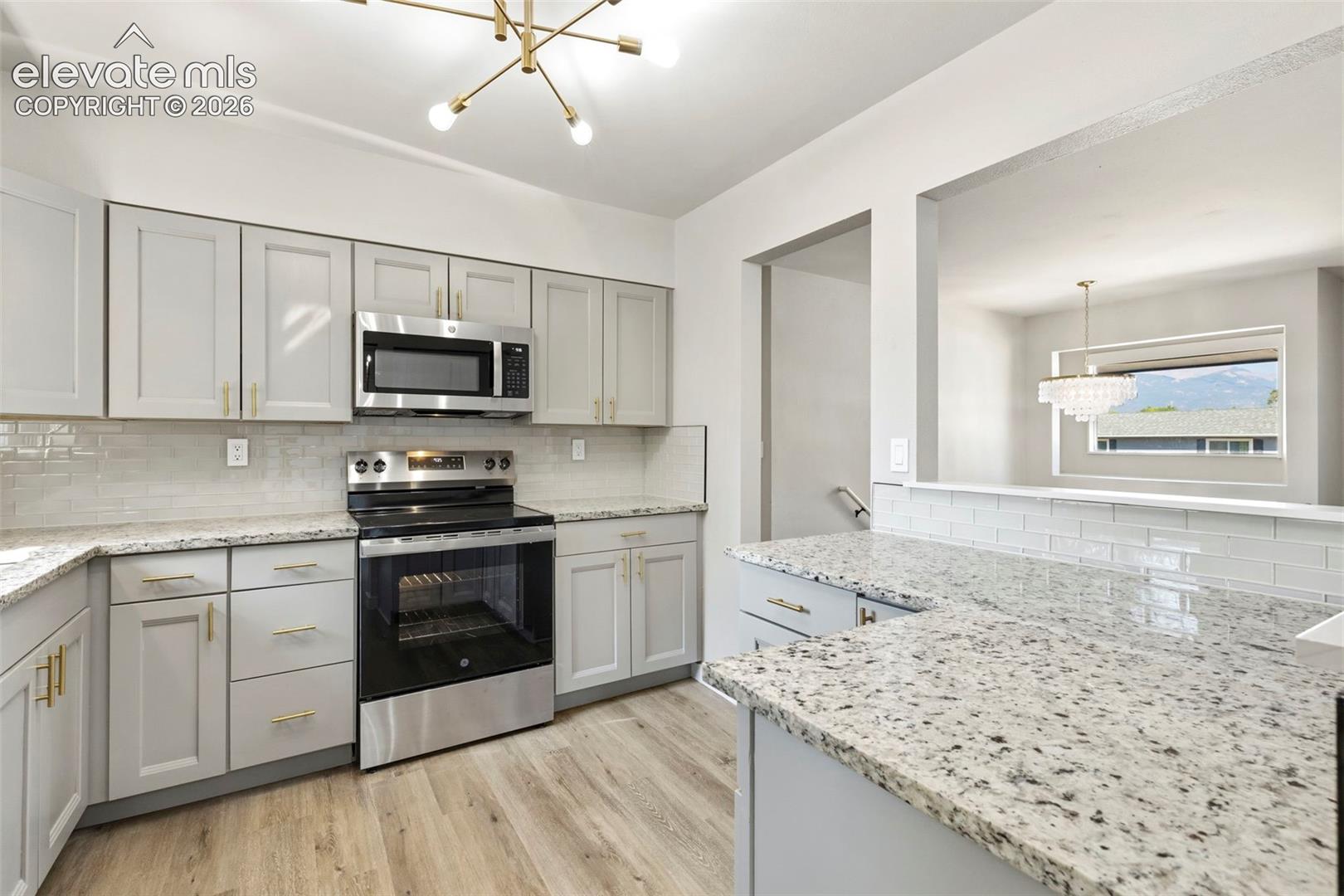 Kitchen featuring gray cabinetry, stainless steel appliances, granite countertops, glass subway tile backsplash, and luxury vinyl plank flooring