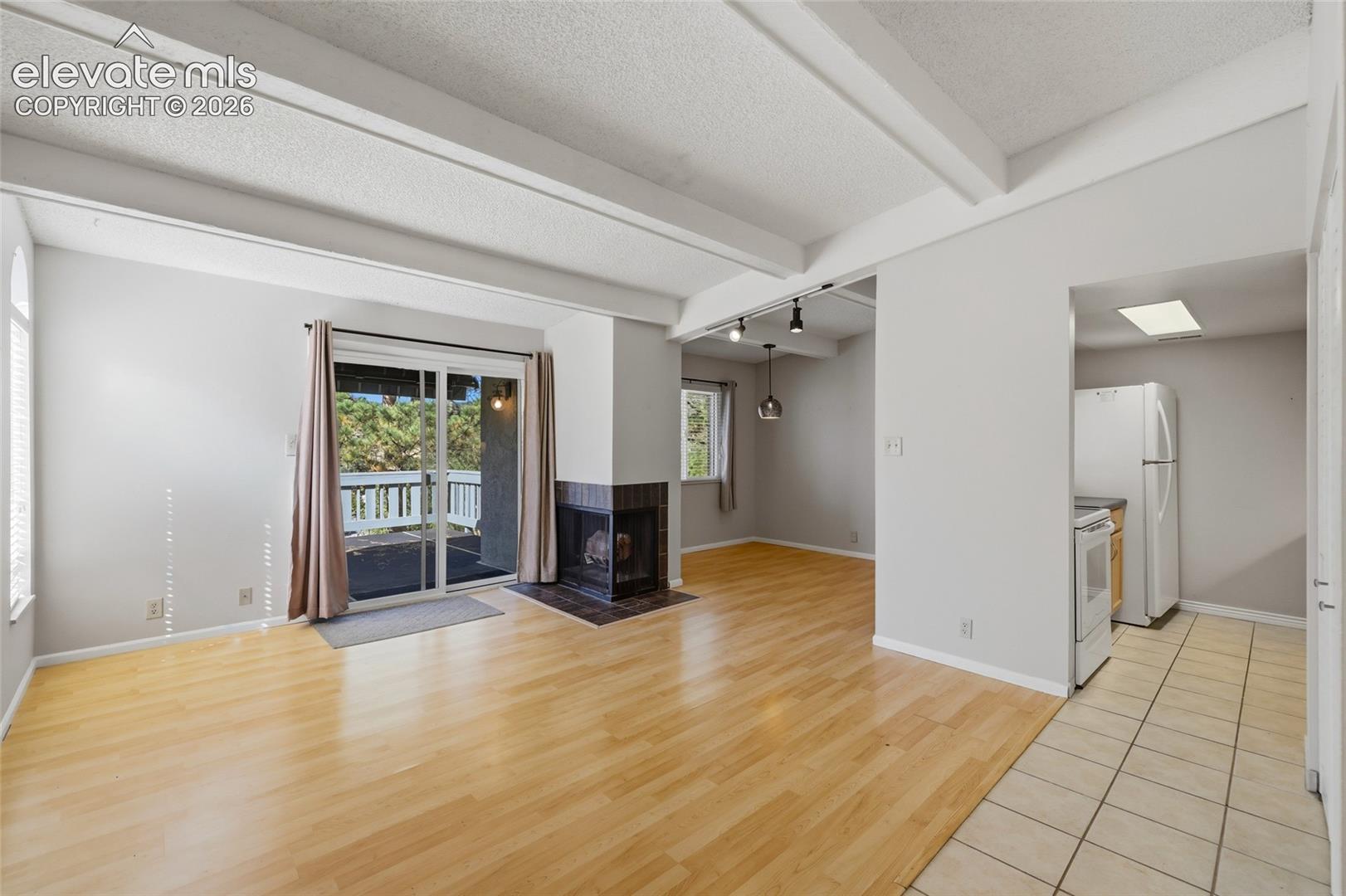 Living area featuring vaulted ceilings with exposed beams, wood-finish flooring, a tile-surround wood fireplace, and an integrated breakfast bar