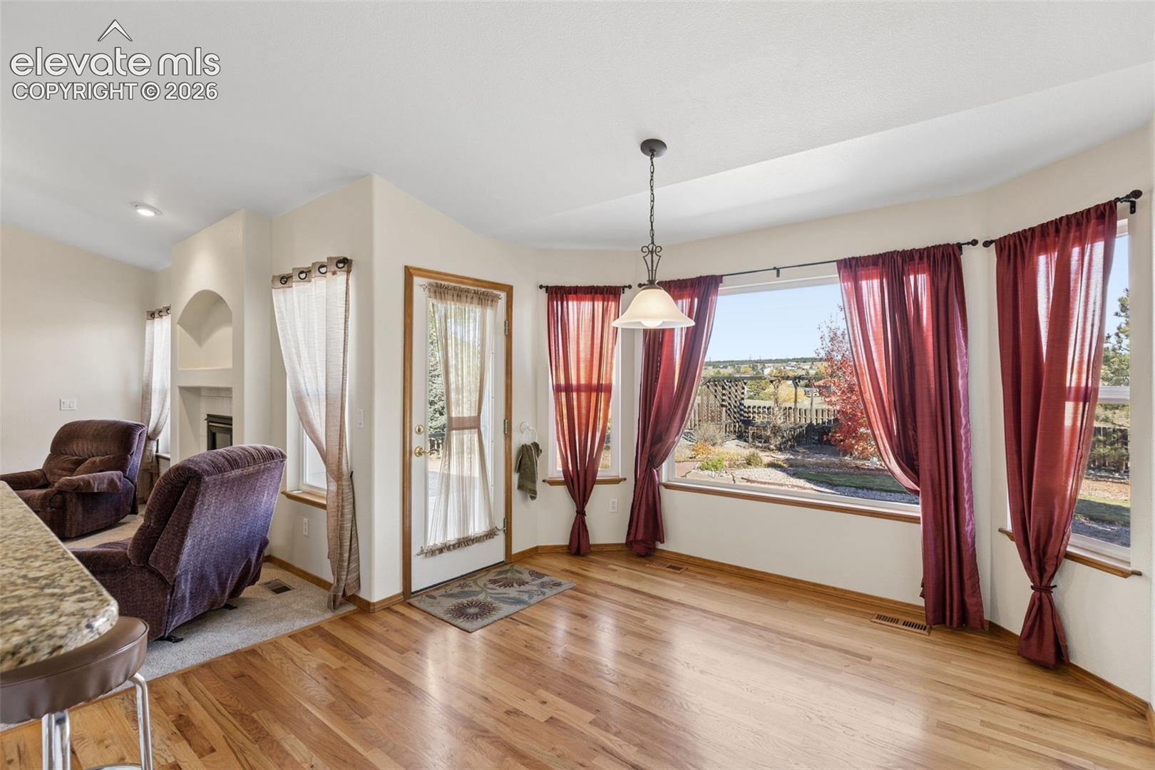 Bay window featuring multi-pane glass, wood-finish flooring, hanging pendant lighting, and a recessed fireplace alcove