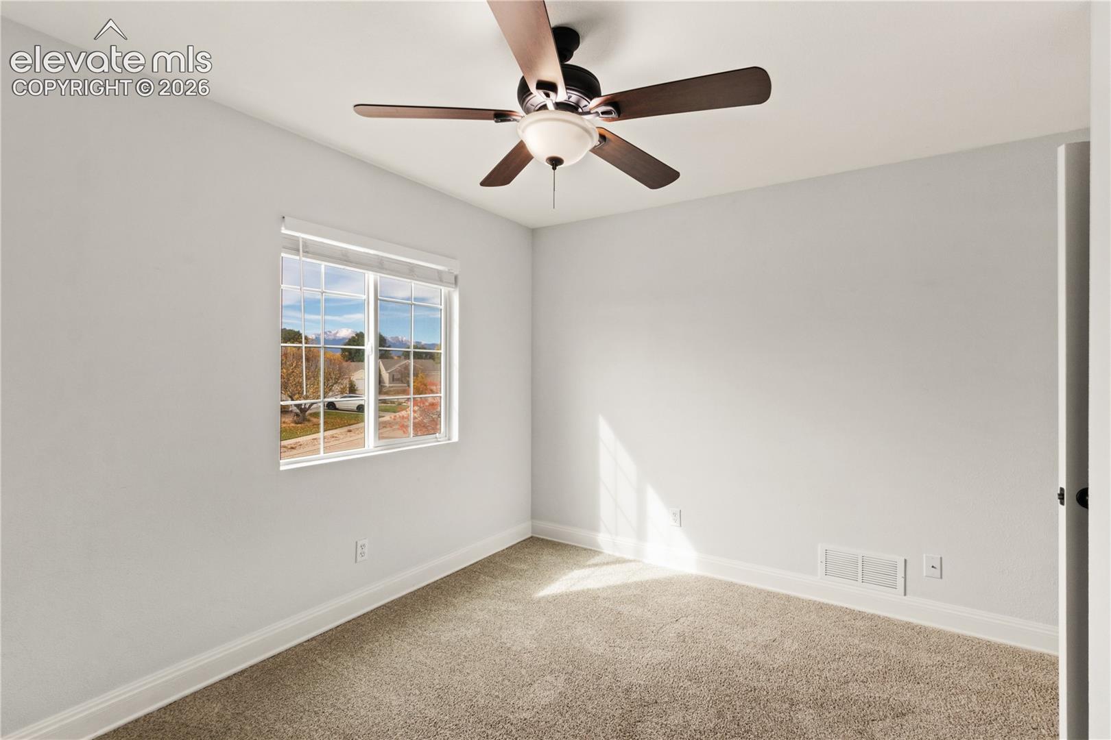 Neutral-toned carpeted flooring, multi-pane window with mountain backdrop, and ceiling-mounted fan with integrated lighting