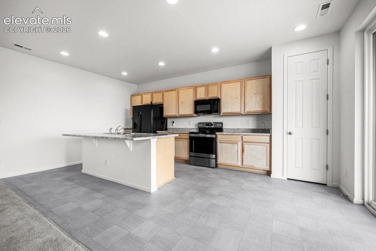 Spacious kitchen featuring natural wood cabinetry, stainless steel appliances, a large center island with extended countertop, recessed ceiling lighting, and slate-finish tile flooring throughout the open layout