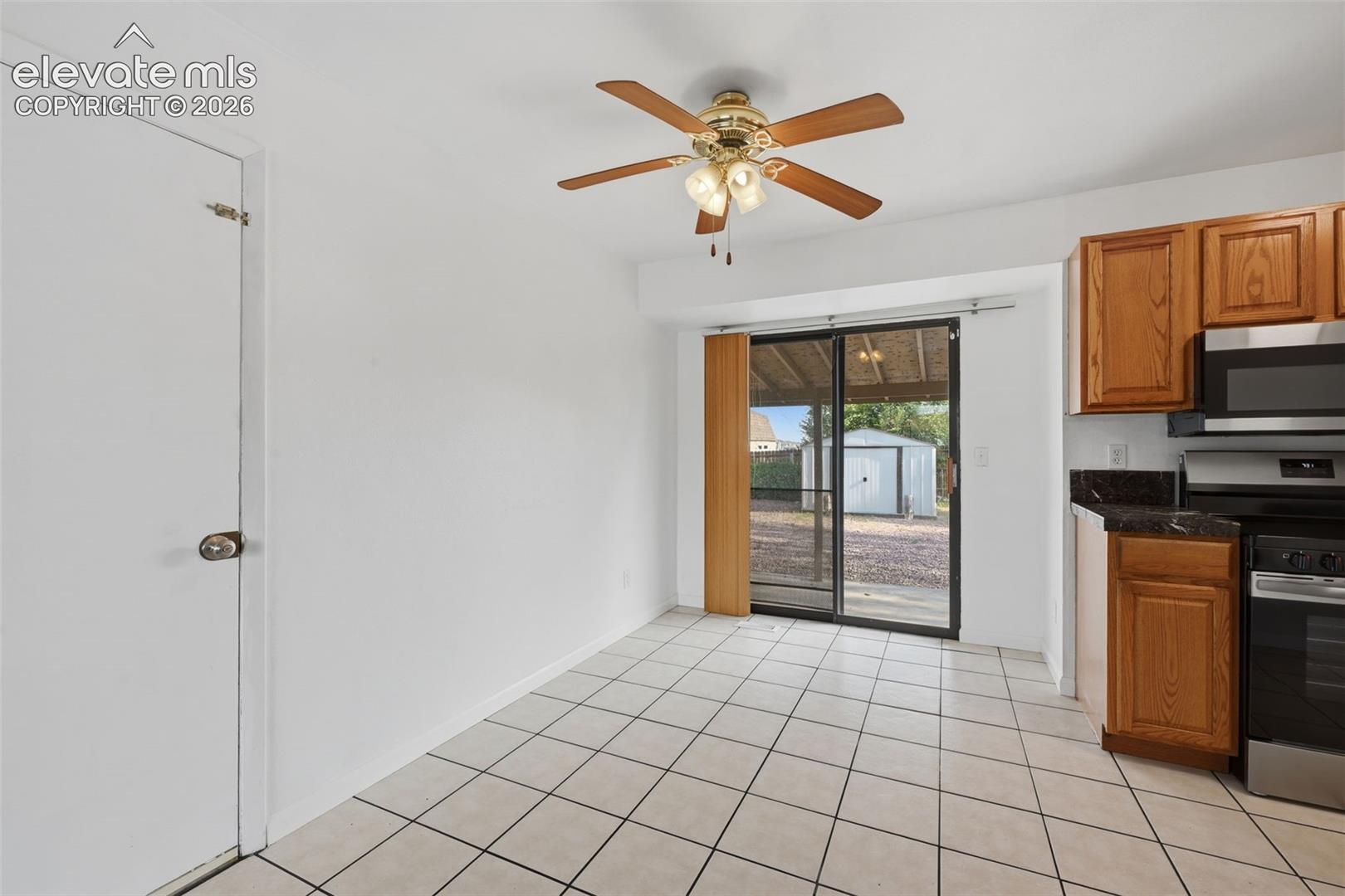 White tile flooring, ceiling fan with light fixture, wood cabinetry, built-in stainless steel microwave, and sliding glass door