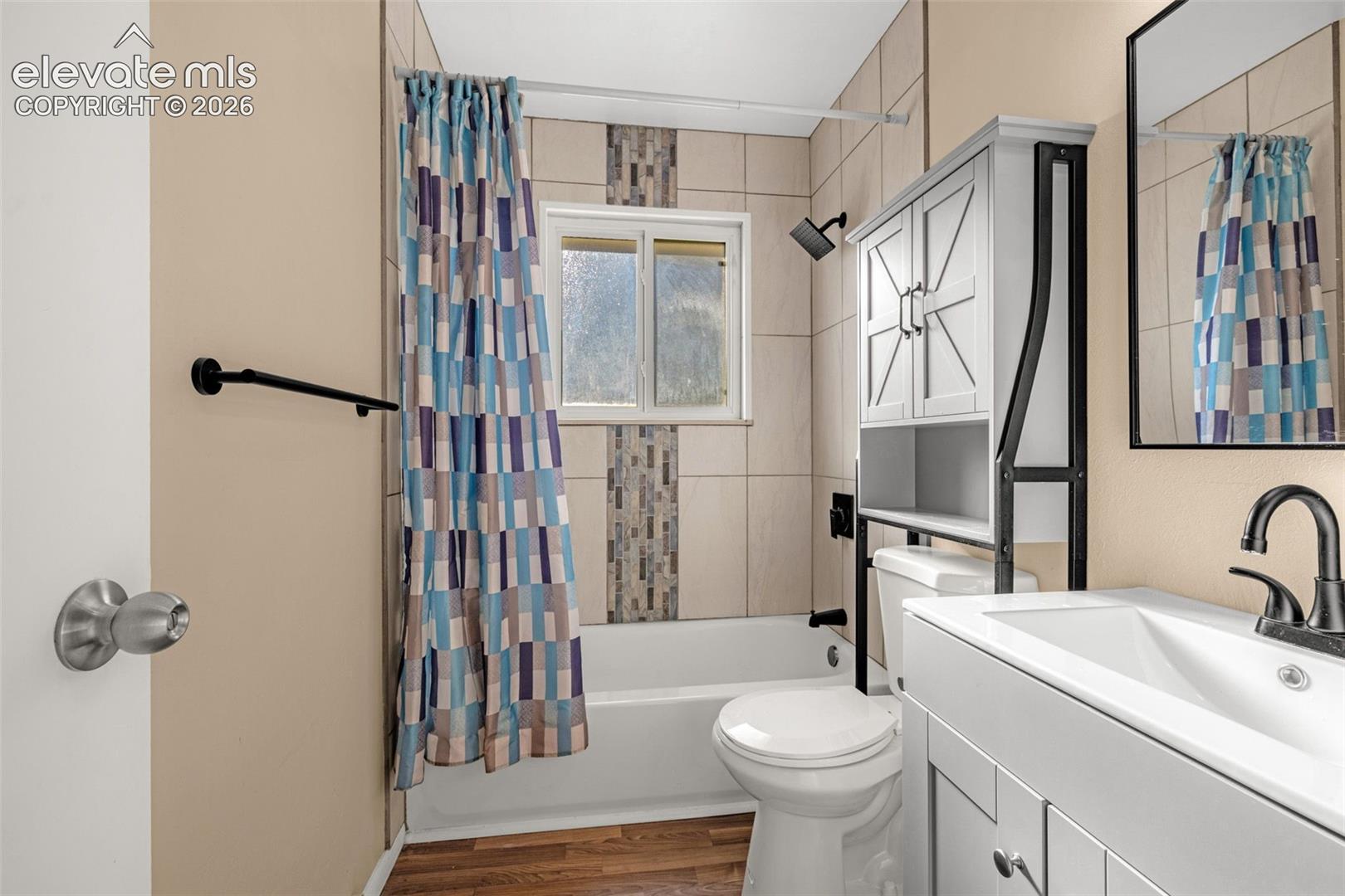 White tub with tile surround, laminate wood-finish flooring, and a window for natural light