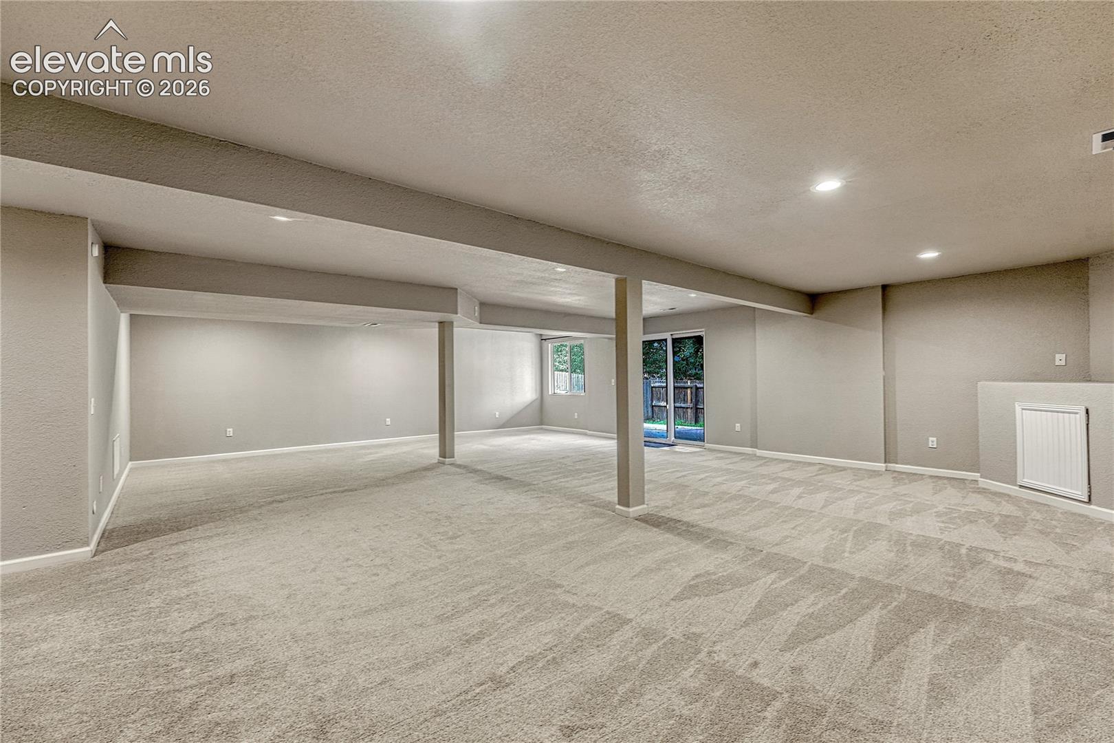 Open-concept floor plan featuring wall-to-wall carpeting, recessed ceiling lighting, a structural support column, and a glass sliding door