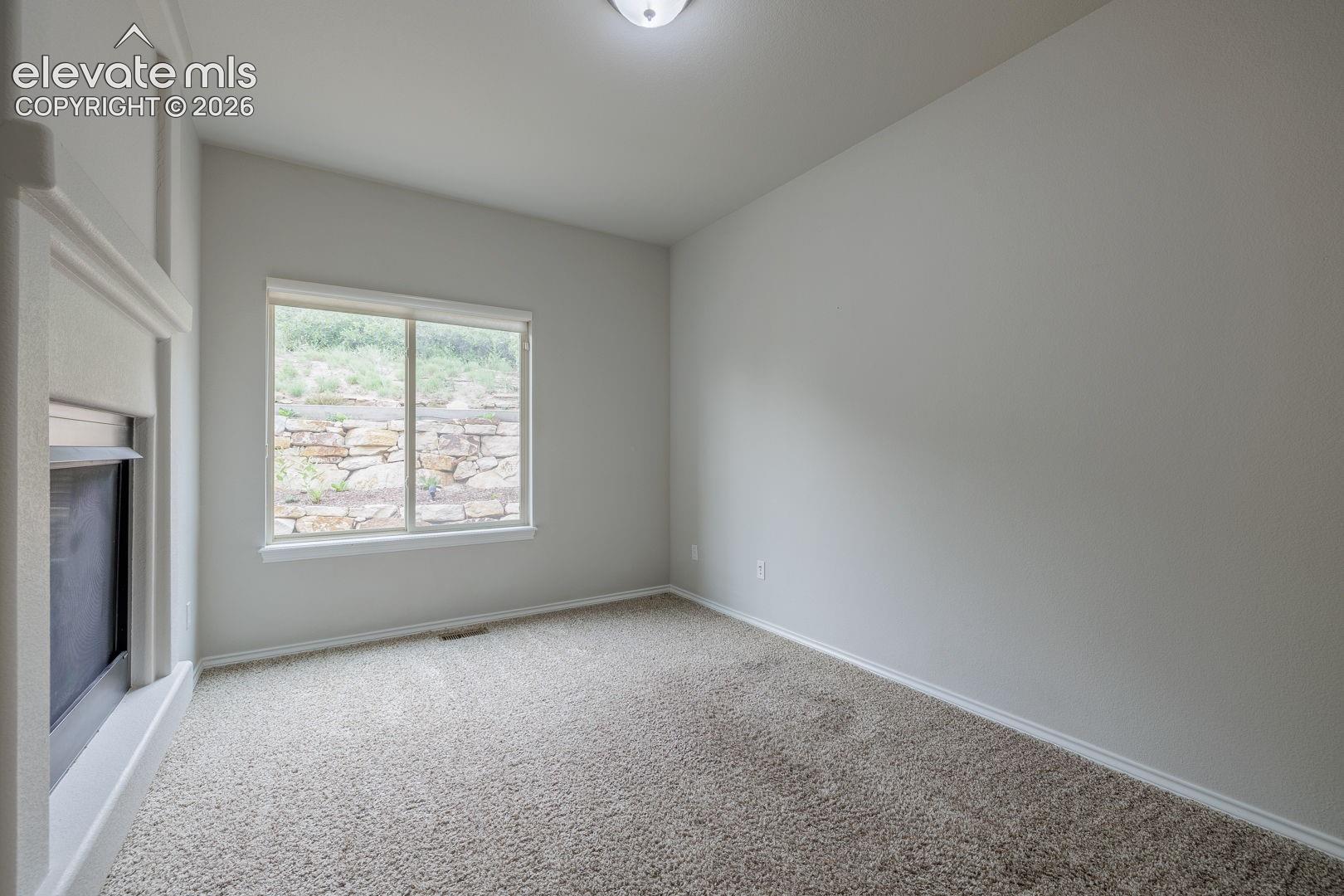 Spacious room with plush carpet flooring, a large window, and a built-in fireplace featuring a white mantel