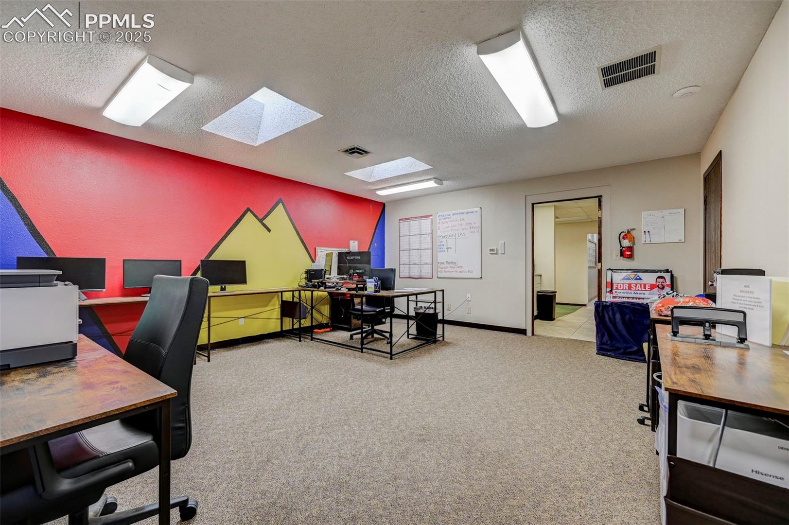Carpeted home office with a skylight, a textured ceiling, and baseboards