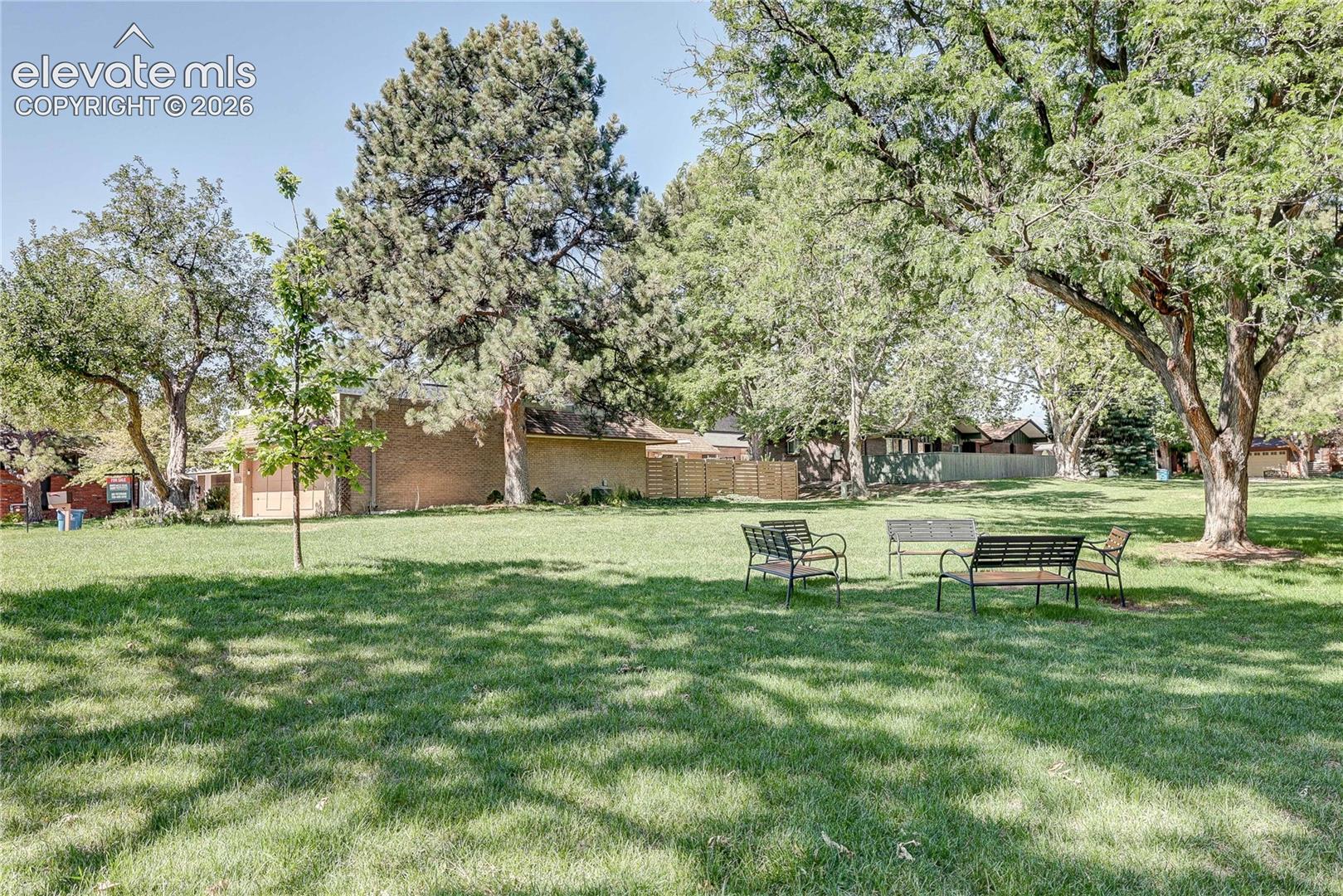 Expansive grounds featuring a manicured lawn, mature trees, and wooden perimeter fencing