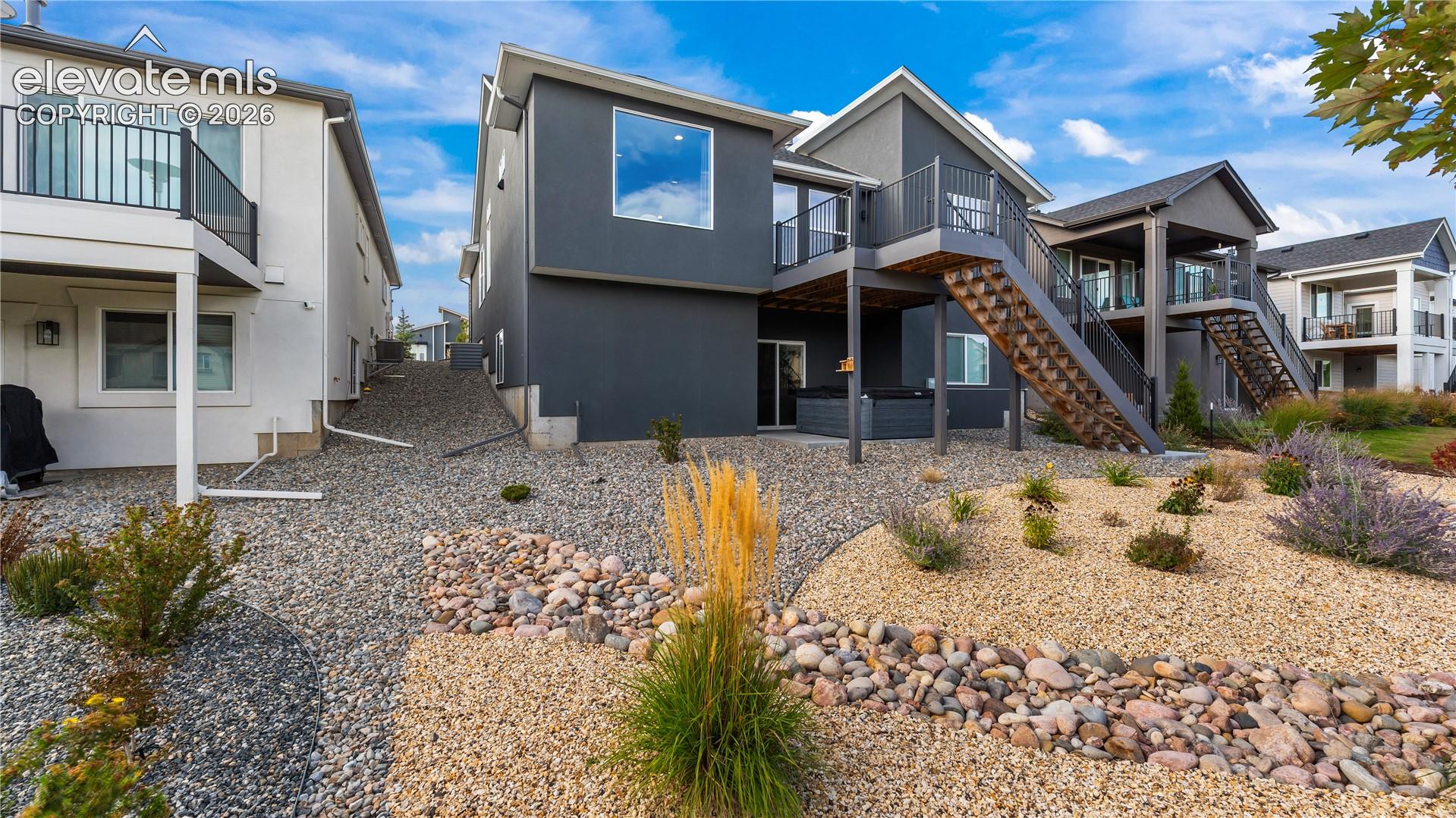Multi-level exterior featuring dark stucco siding, a raised deck with metal railings, external stairs, and low-maintenance rock landscaping
