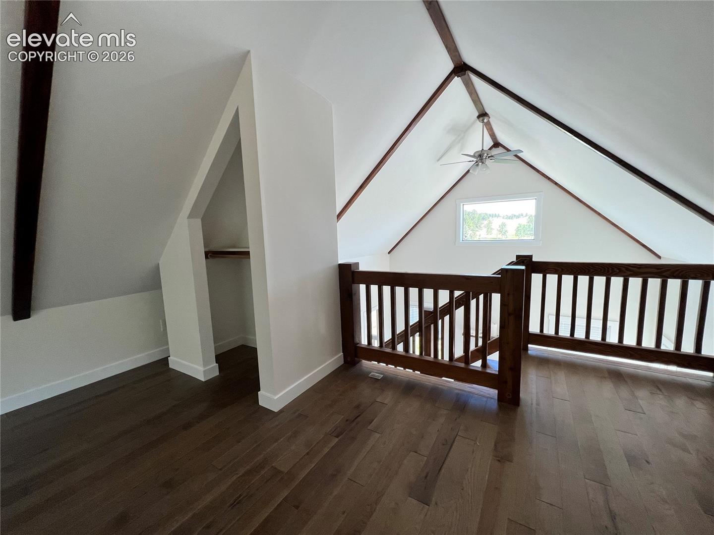 Vaulted ceiling with exposed wood beams, wood-finish flooring, wood railing, built-in open shelving, and a ceiling fan