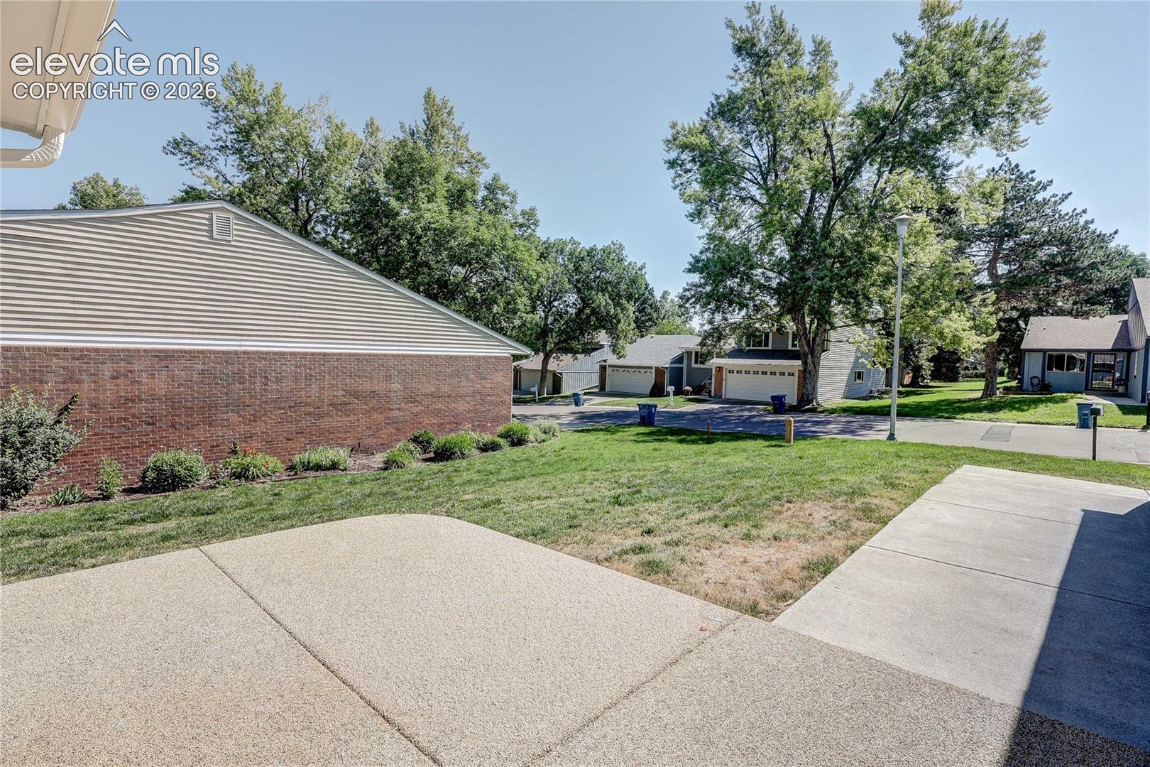 Concrete patio slab featuring a brick and horizontal siding exterior, mature trees, and expansive lawn area