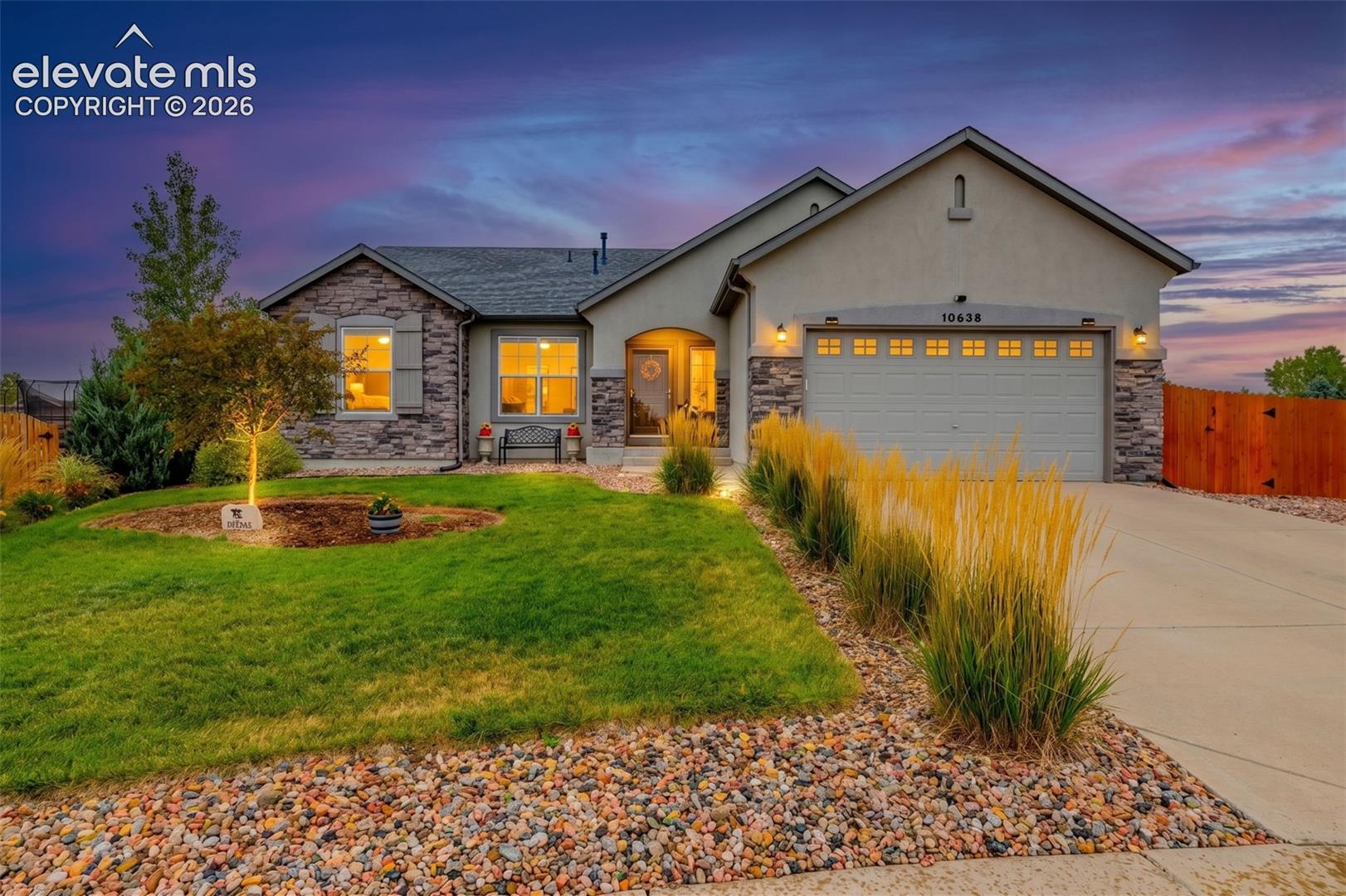 Single-story residence featuring a stone and stucco facade, an attached three-car garage, and landscaped front yard with decorative stone ground cover