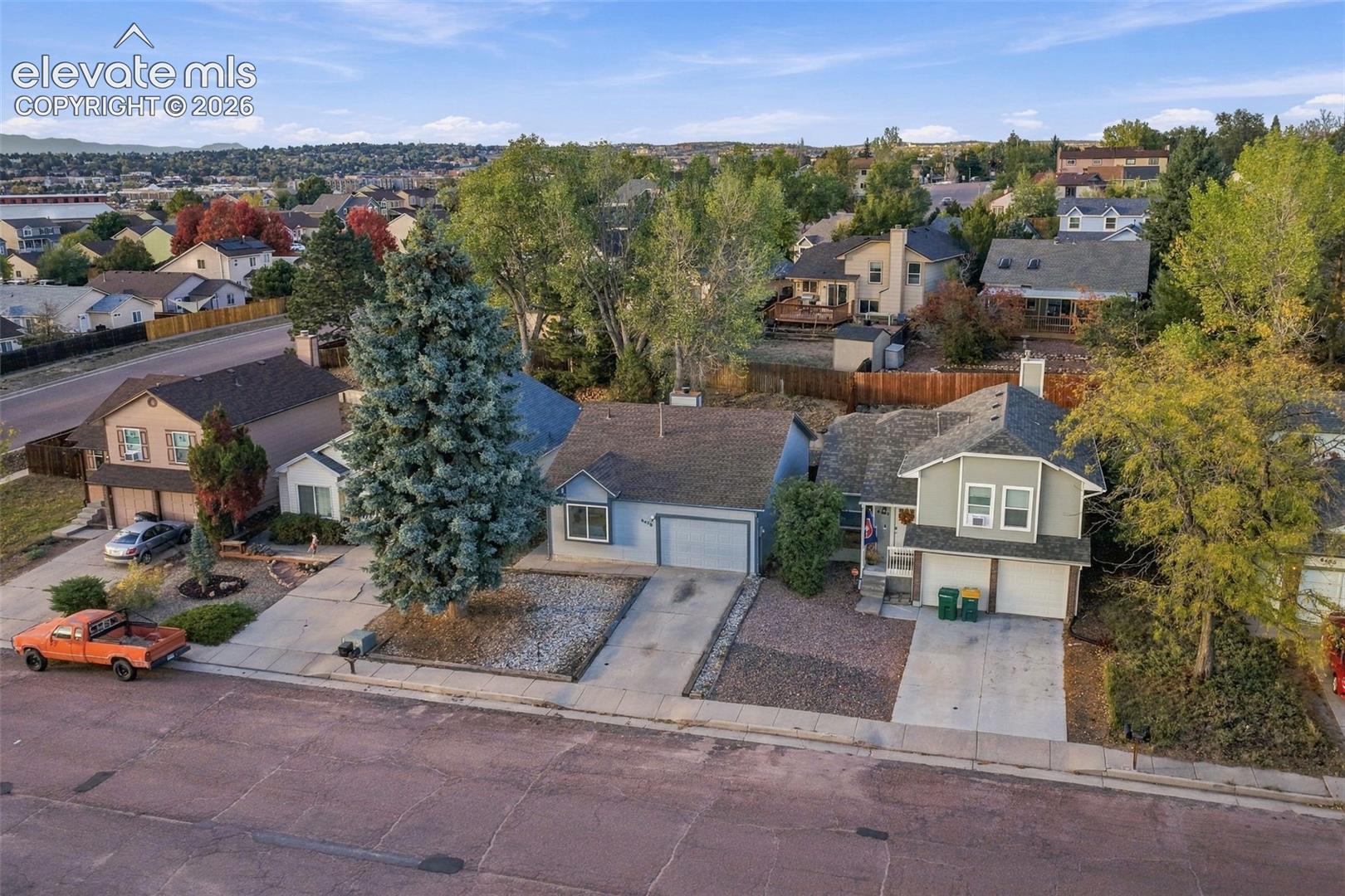 Aerial perspective of the residential property featuring an asphalt-shingle roof, attached garage, concrete driveway, and mature landscaping
