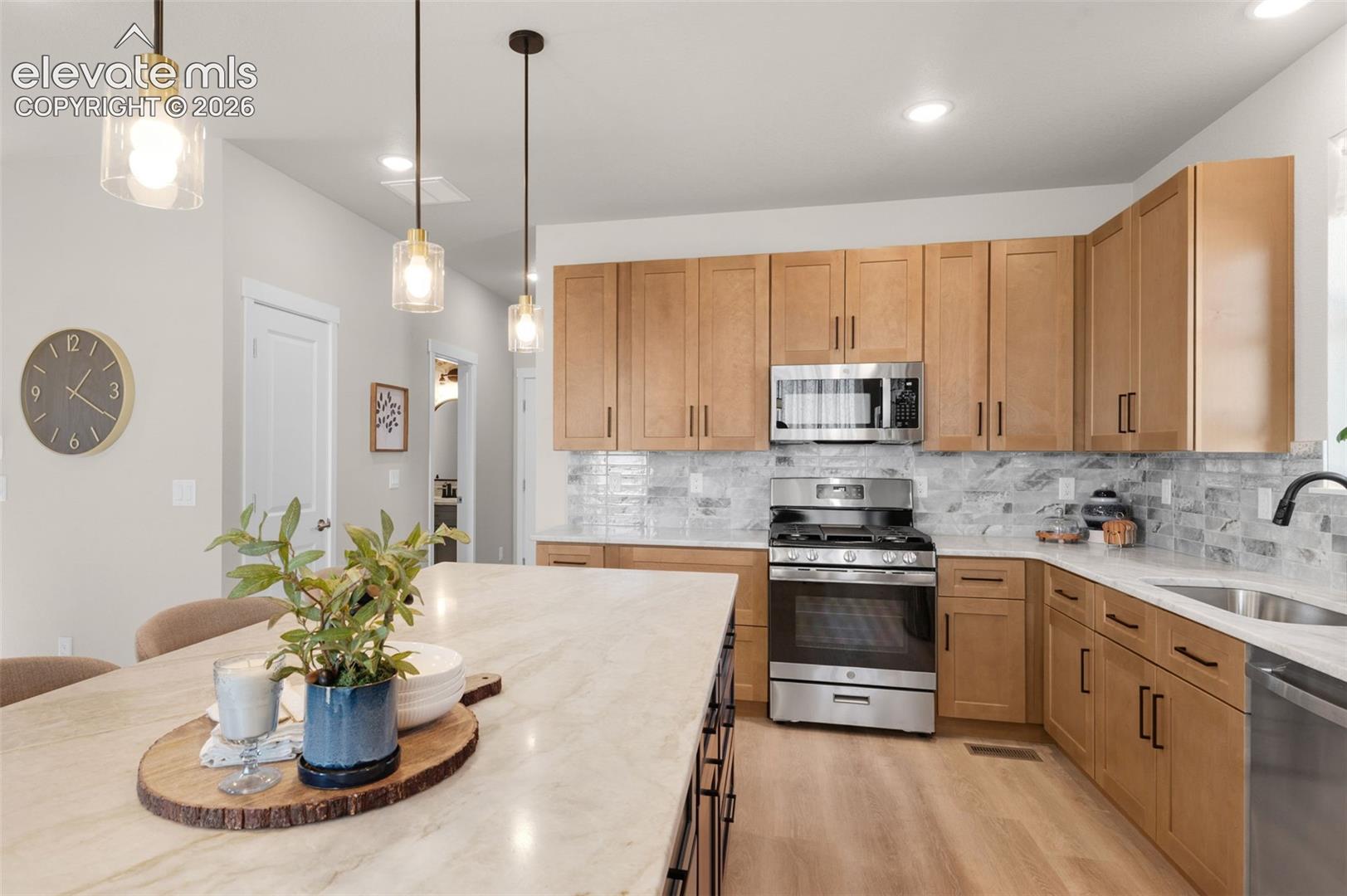 Kitchen featuring wood-finish cabinetry, stainless steel appliances, a tiled backsplash, and pendant lighting