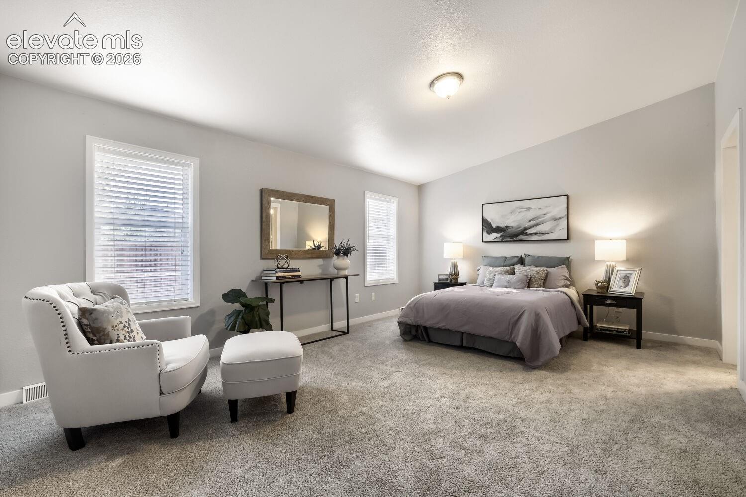 Spacious room featuring neutral wall paint, carpeting, vaulted ceilings, and dual windows with horizontal blinds