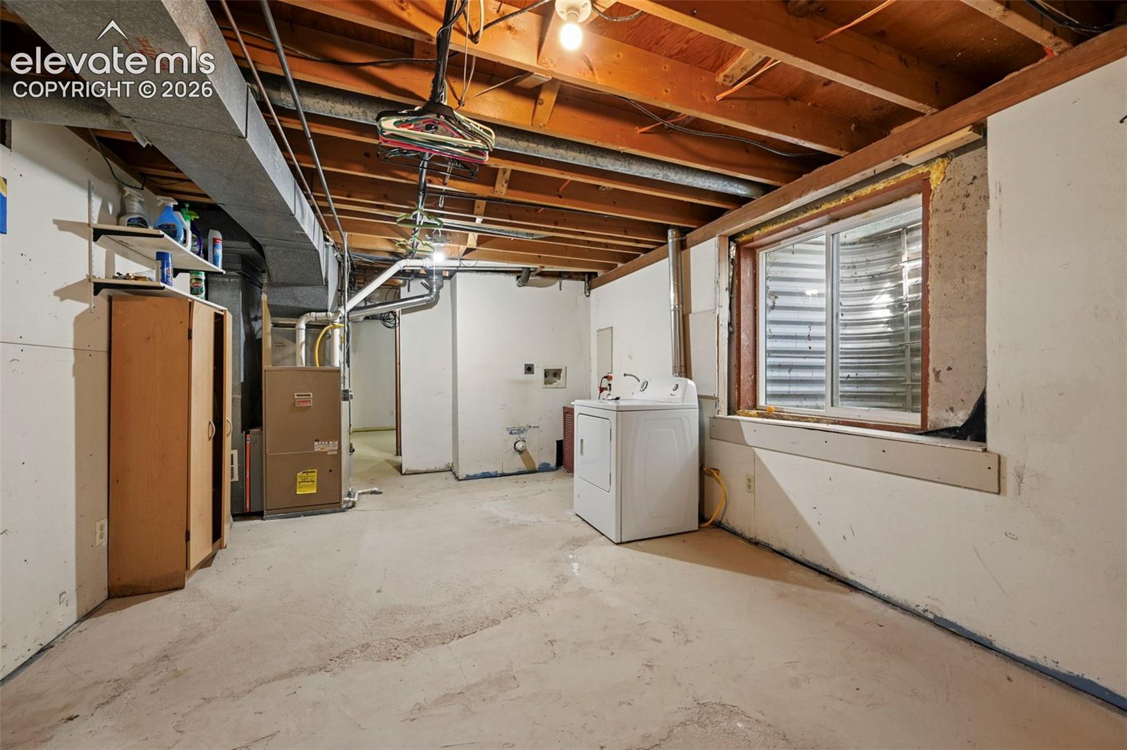 Open basement area featuring concrete flooring, exposed ceiling joists, and a utility window