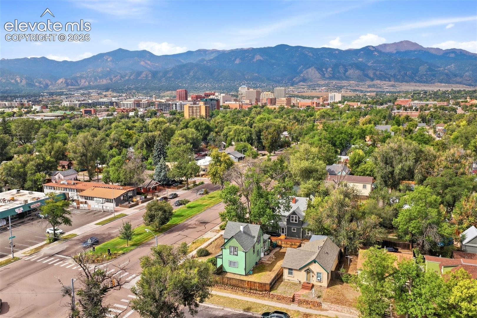 Expansive mountain backdrop, urban skyline, mature trees, residential street, and commercial buildings