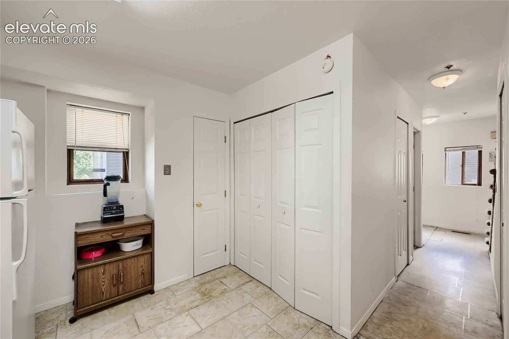 Tile flooring, white paneled bifold doors, white paneled door, and a single window with blinds