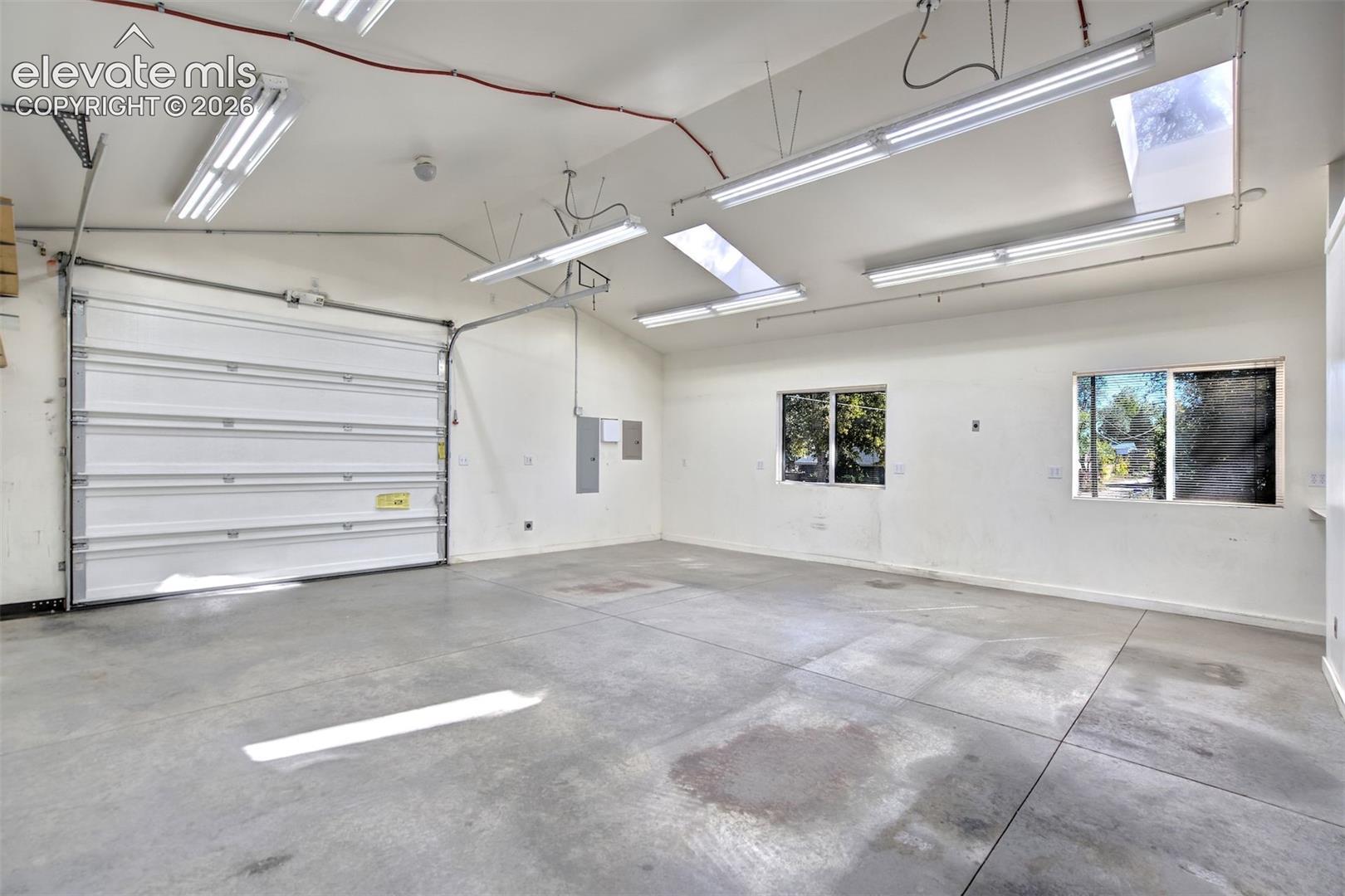 Spacious garage featuring concrete flooring, a sectional overhead door, skylights, multiple high-output light fixtures, and dual windows