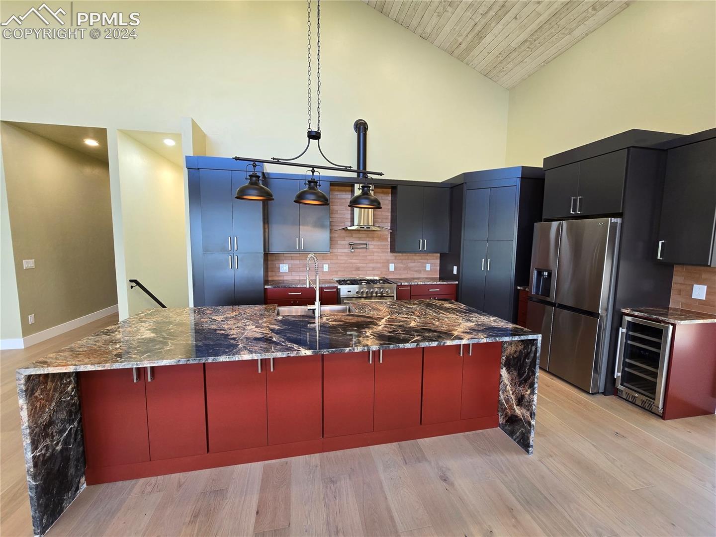 Kitchen featuring a large island with sink, backsplash, wine cooler, hanging light fixtures, and appliances with stainless steel finishes