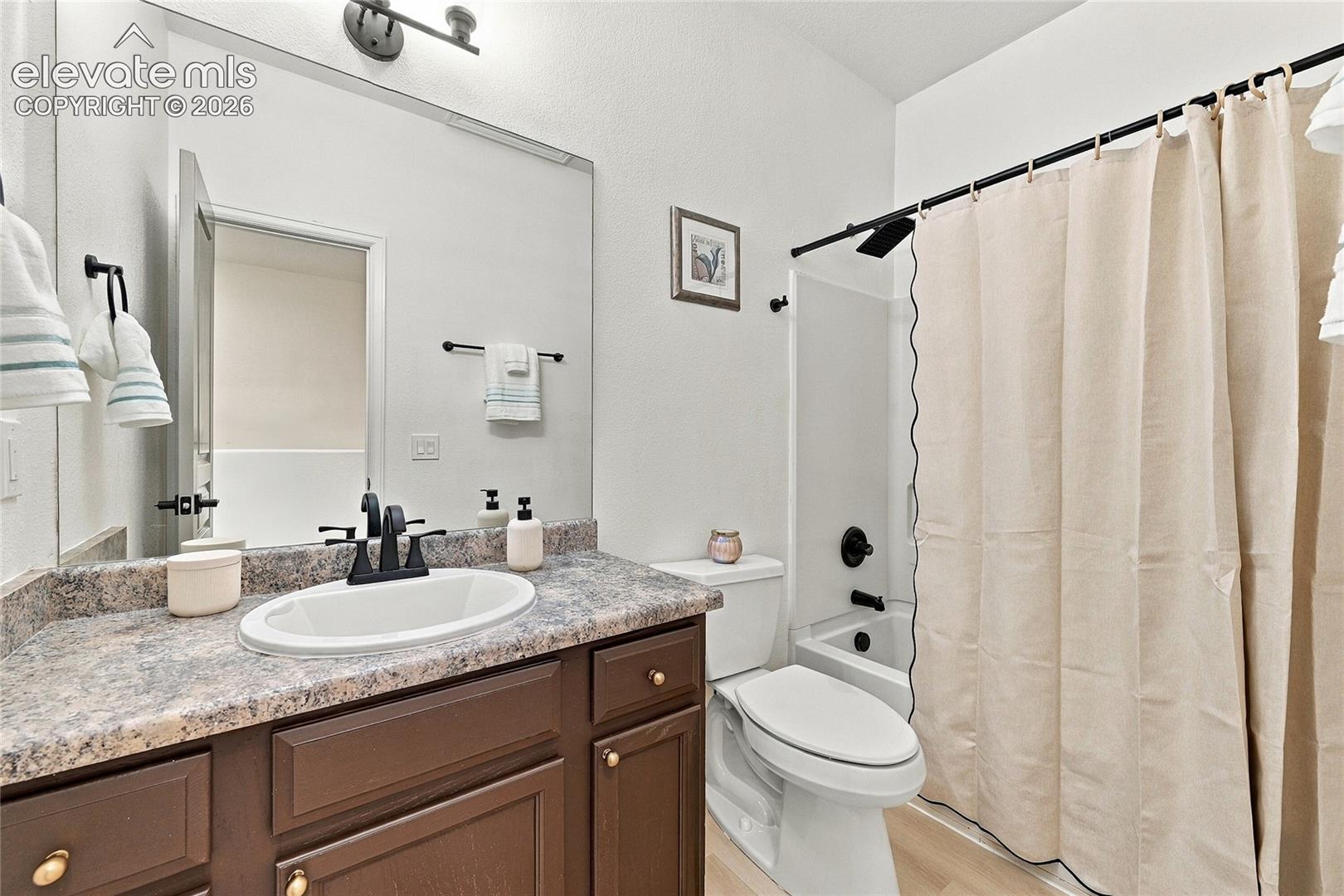 Bathroom featuring a vanity with wood-finish cabinetry, patterned laminate countertop, white oval undermount sink, matte black faucet hardware, and a tub-shower combination