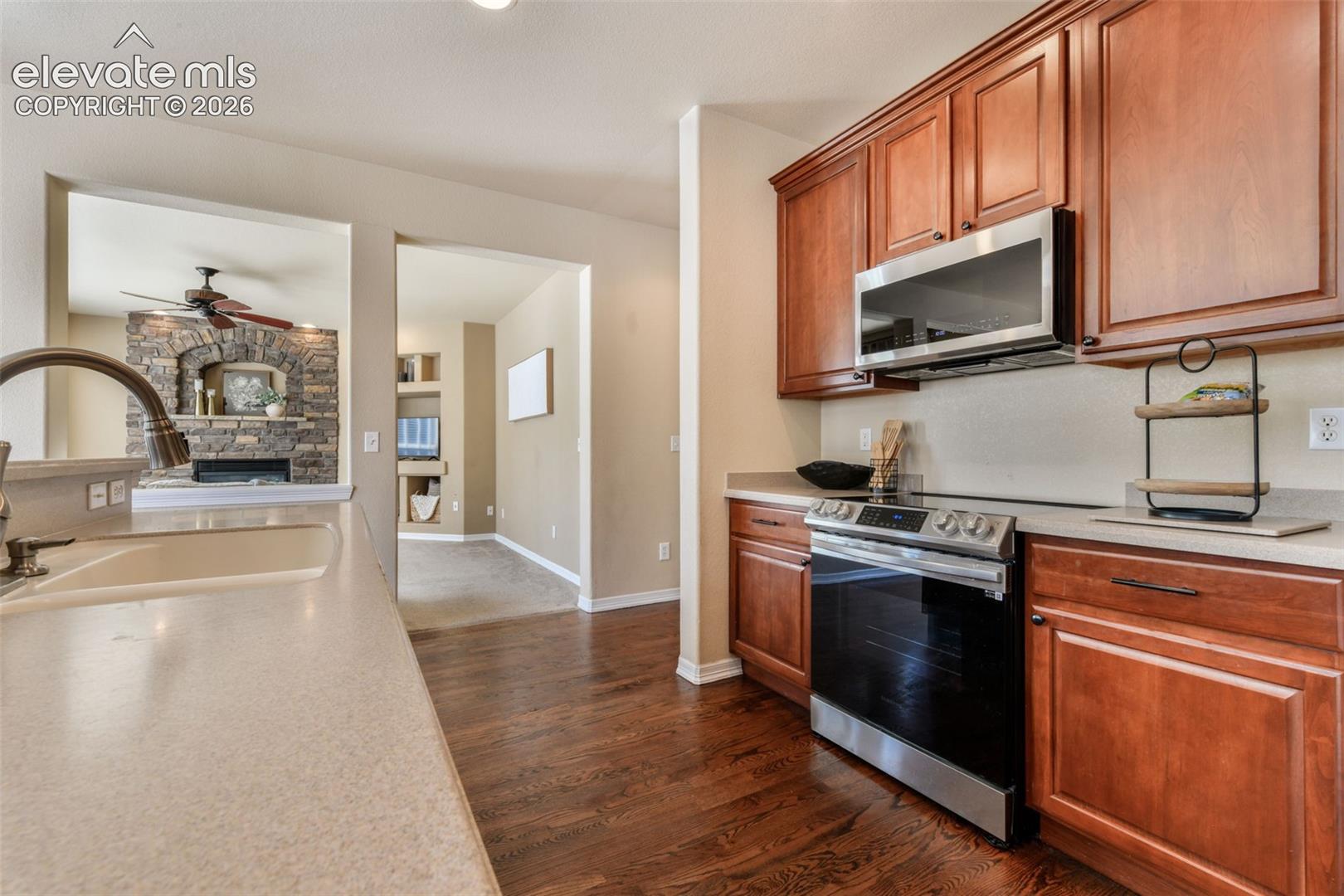 Well-appointed kitchen featuring wood-finish flooring, cherry-toned cabinetry, stainless steel appliances, and solid surface countertops