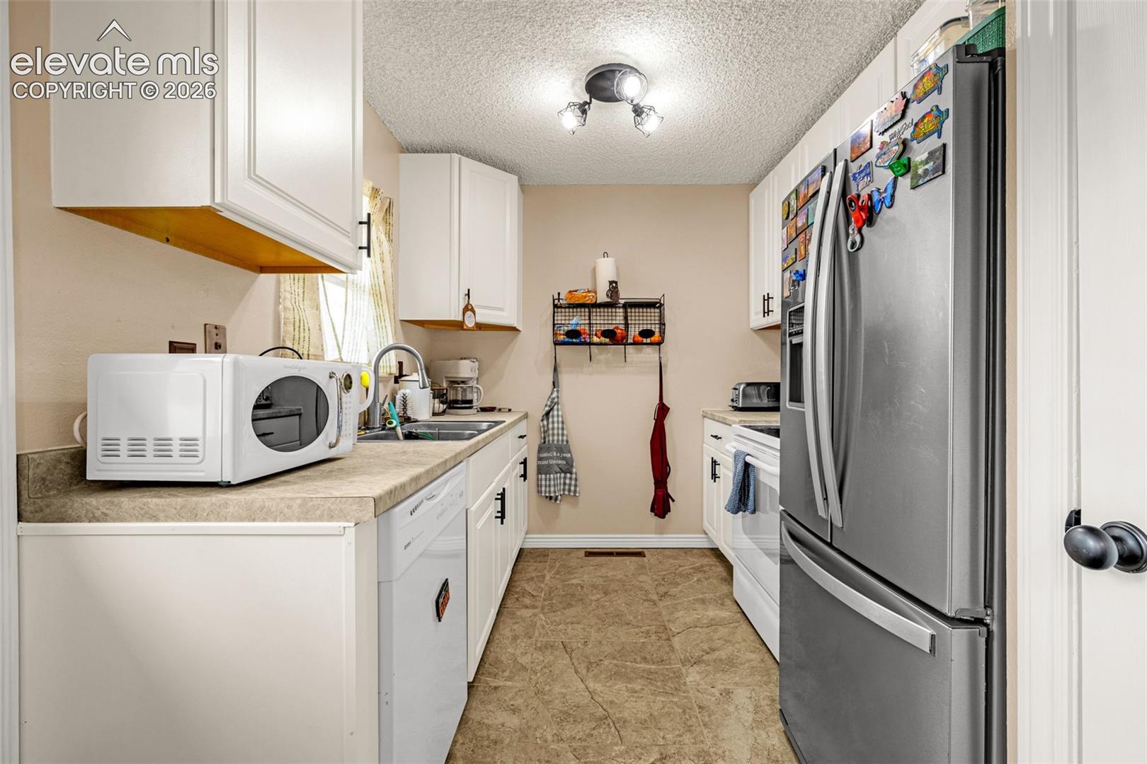 Kitchen featuring white cabinetry with black hardware, stainless steel refrigerator, white dishwasher, dual-basin sink with a gooseneck faucet, and tile flooring