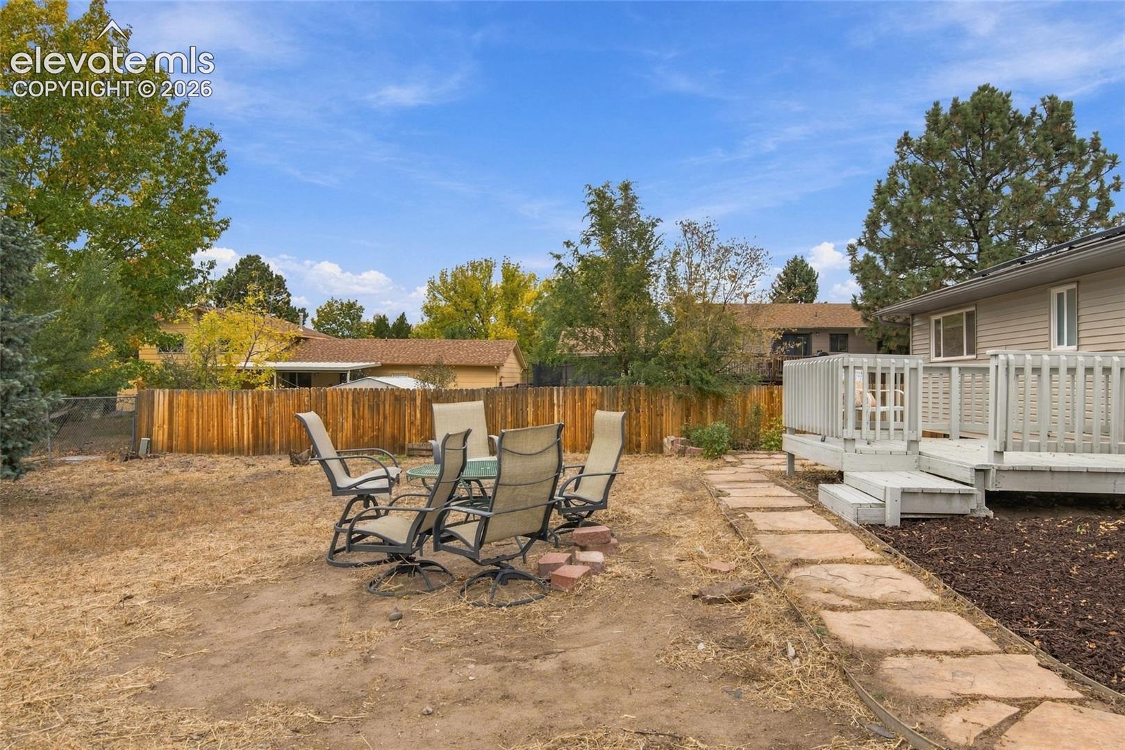 Backyard featuring a raised wooden deck, stone paver pathway, wood privacy fencing, and mature trees