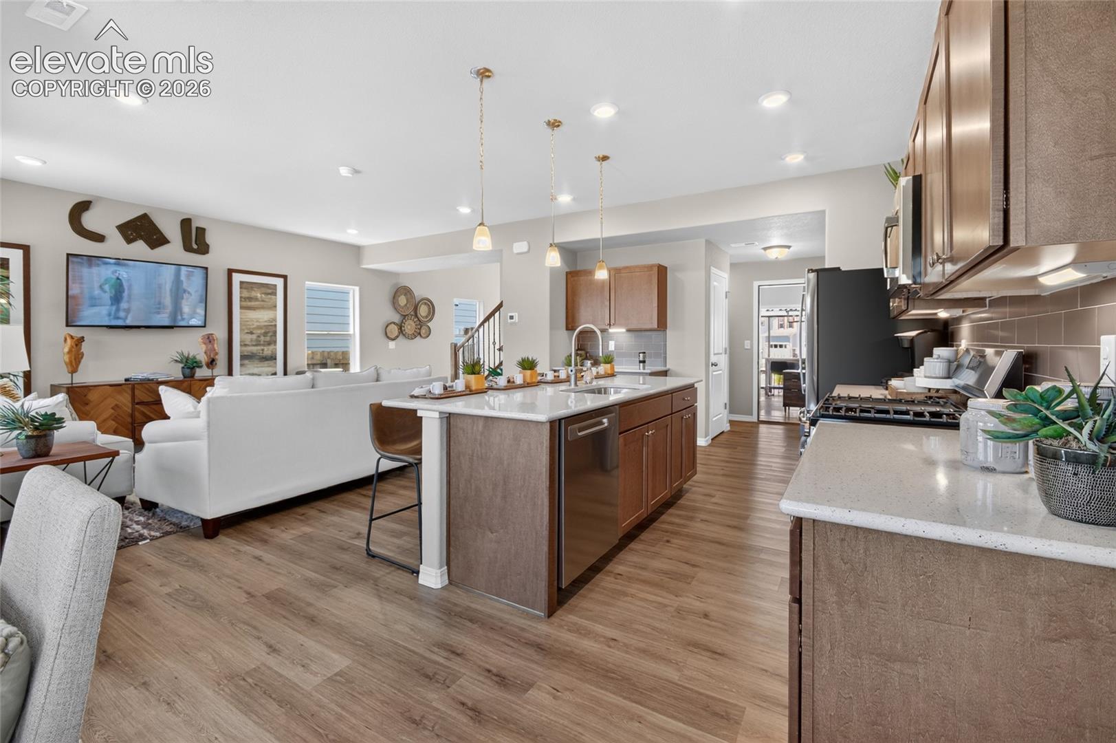 Kitchen featuring wood-finish cabinetry, stone-composite countertops, stainless steel appliances, a center island with pendant lighting, and wood-finish flooring