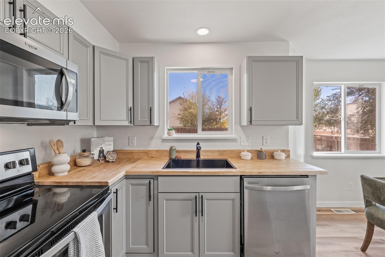Kitchen featuring light gray shaker-style cabinetry, wood-finish countertops, stainless steel appliances, a black undermount sink with a matte black faucet, and recessed lighting
