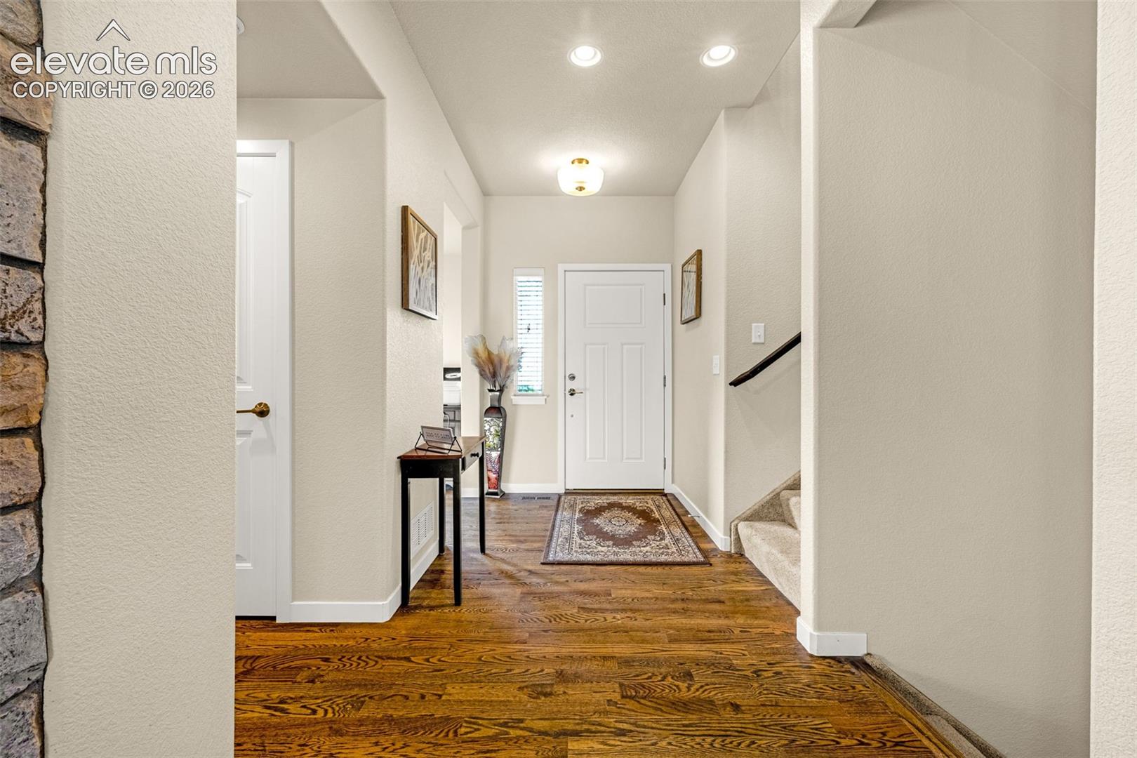 Entryway featuring wood-finish flooring, a stone-accented wall, recessed ceiling lighting, a flush-mount light fixture, and a staircase with a handrail