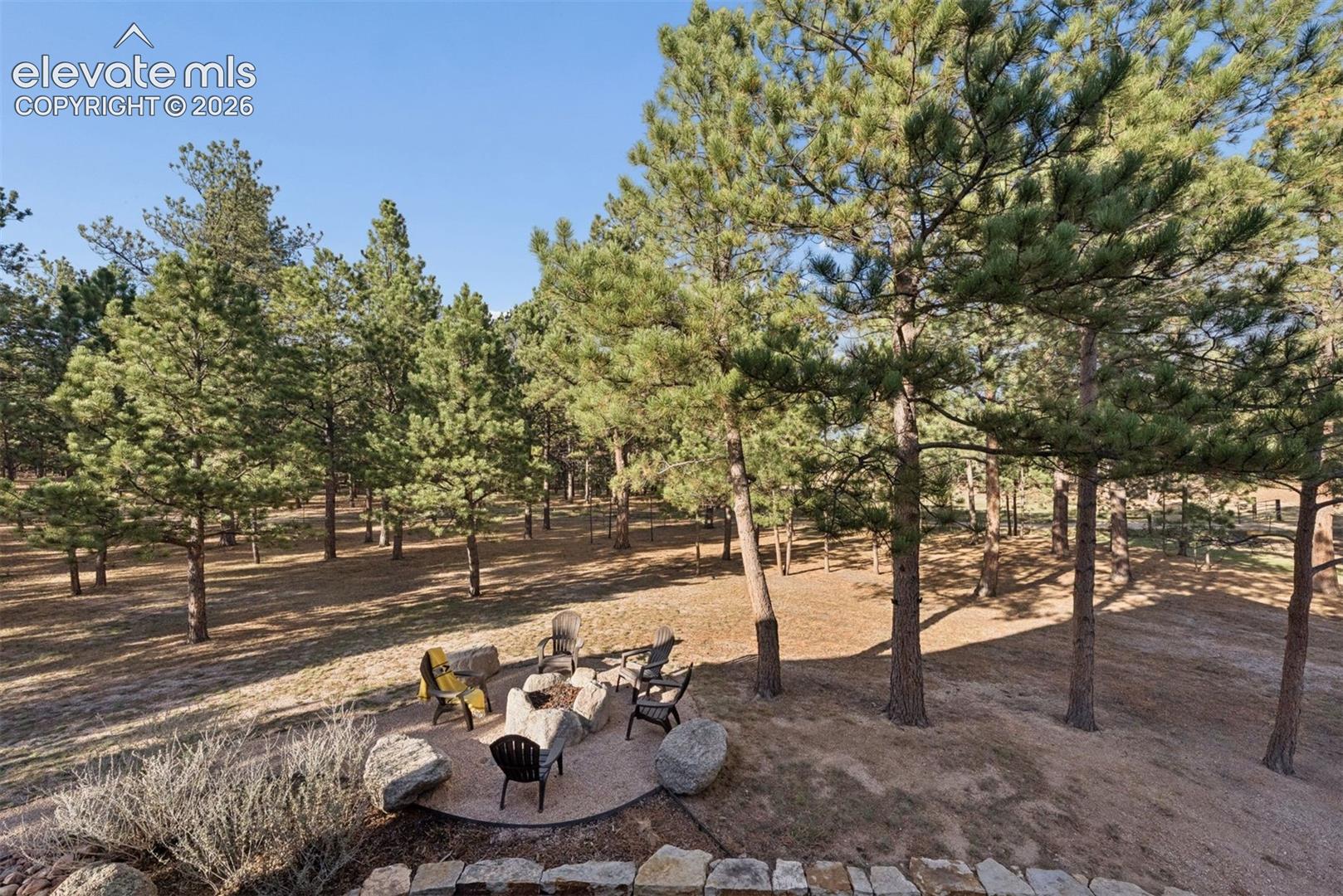 Outdoor grounds featuring a circular gravel fire pit area, boulder hardscaping, and mature pine trees