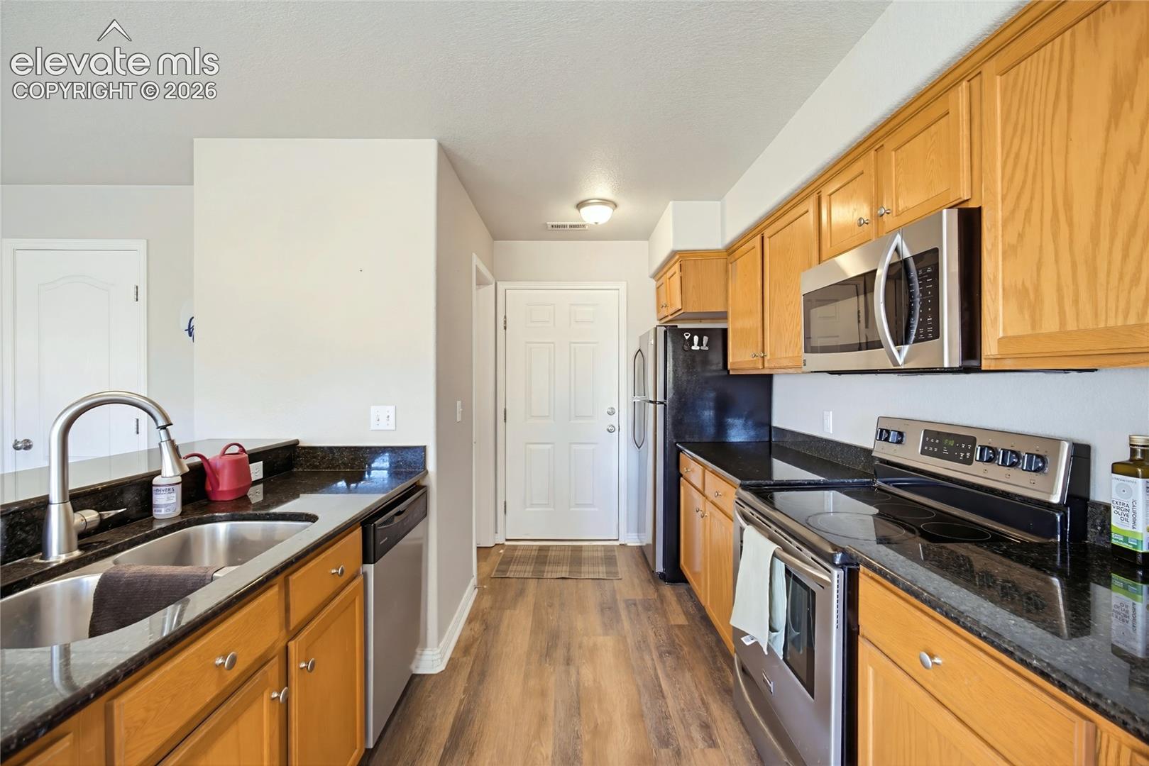 Kitchen featuring wood-finish cabinetry, dark stone countertops, stainless steel appliances, and a stainless steel undermount sink with a gooseneck faucet