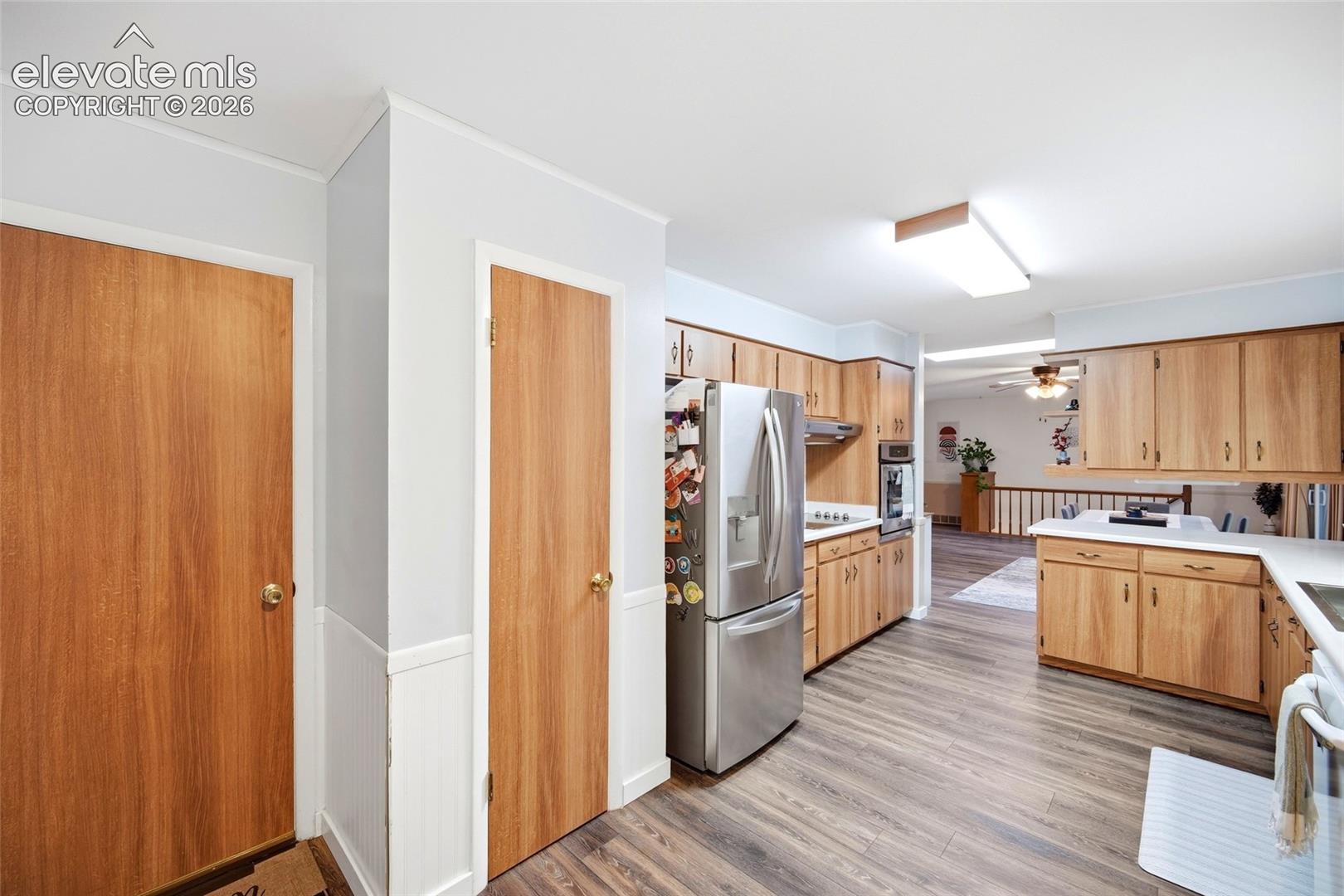 Kitchen featuring wood-finish cabinetry, stainless steel refrigerator, built-in wall oven, and wood-finish flooring
