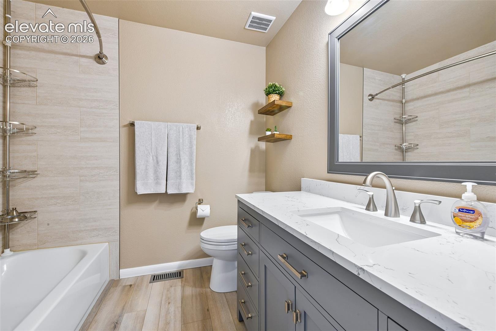 White bathtub with tile surround, wood-finish flooring, and a gray vanity with a white countertop