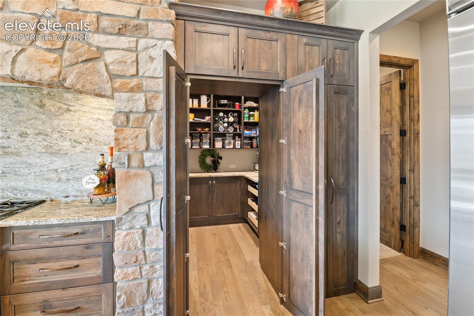 Concealed entry to oversized walk-in pantry with custom cabinetry, blending seamlessly into the kitchen's stone and wood design.