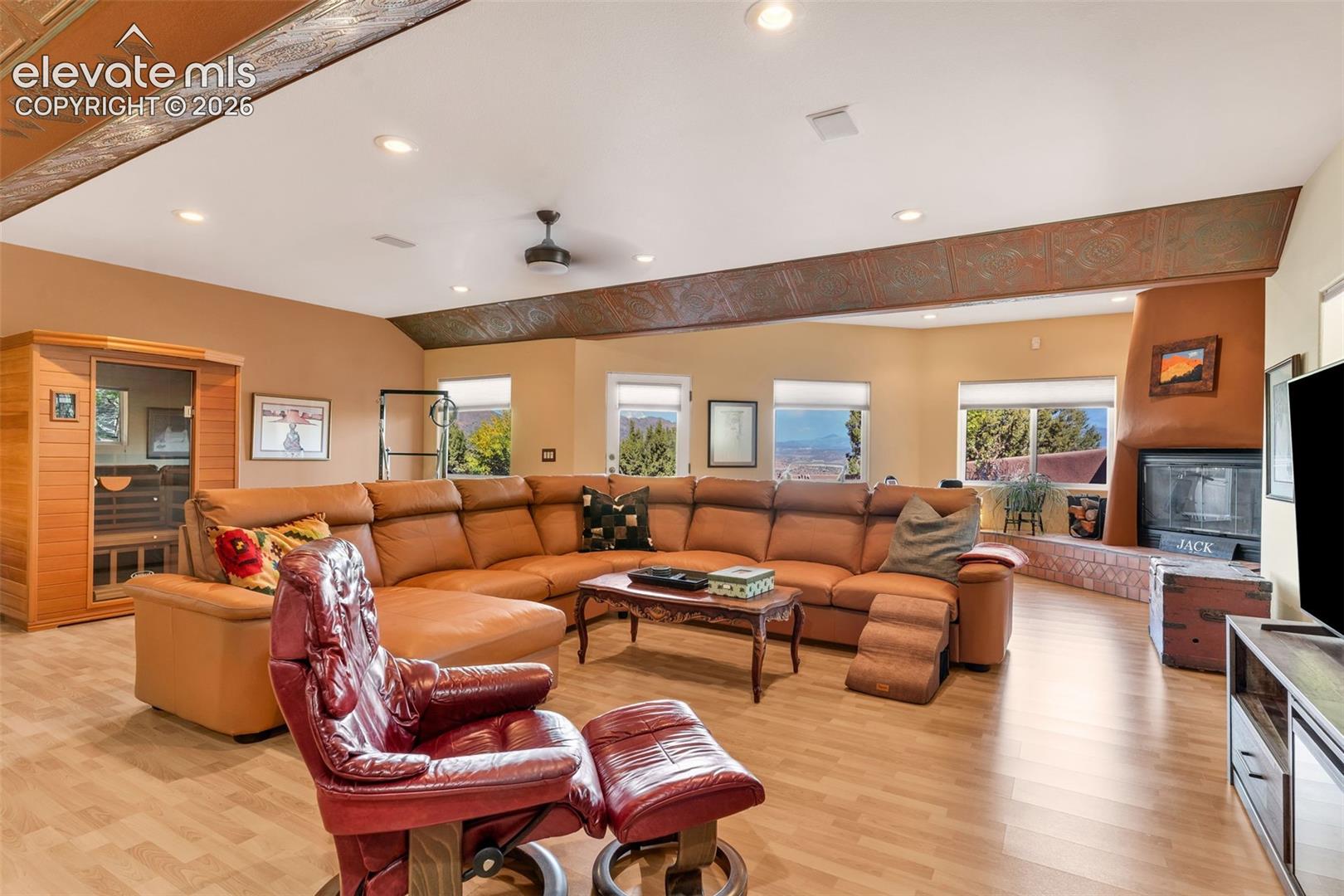 Living area featuring recessed lighting, a vaulted ceiling with decorative metal soffit detailing, wood-finish flooring, a kiva-style fireplace with tile hearth, and a built-in sauna